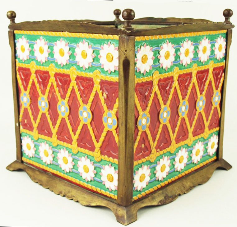 A very rare Minton Majolica planter designed as four: A very rare Minton Majolica planter designed as four tiles decorated with orange trellis and a frieze of stylized daisy heads to the top edge, all on a red ground, set in a brass frame with ball finia