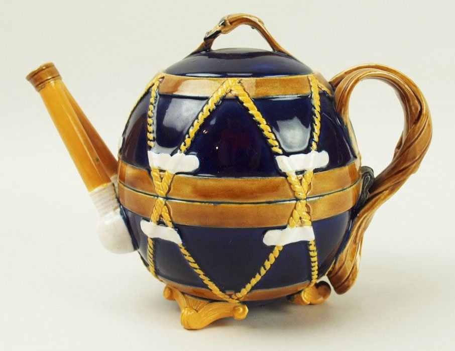 A rare George Jones ‘Drum’ teapot c.1875, the cobalt: A rare George Jones ‘Drum’ teapot c.1875, the cobalt blue body decorated with orange rope drum skin tighteners, a leather carrying strap forming the handle and two drumsticks to form the spout. Th
