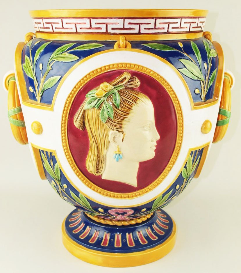 An Elegant Minton Majolica jardiniere c.1865, modeled: An Elegant Minton Majolica jardiniere c.1865, modeled as an ovoid vase with two oval panels with maidens heads emblematic of Europe and Asia against a red ground, two large orange glazed ring handles