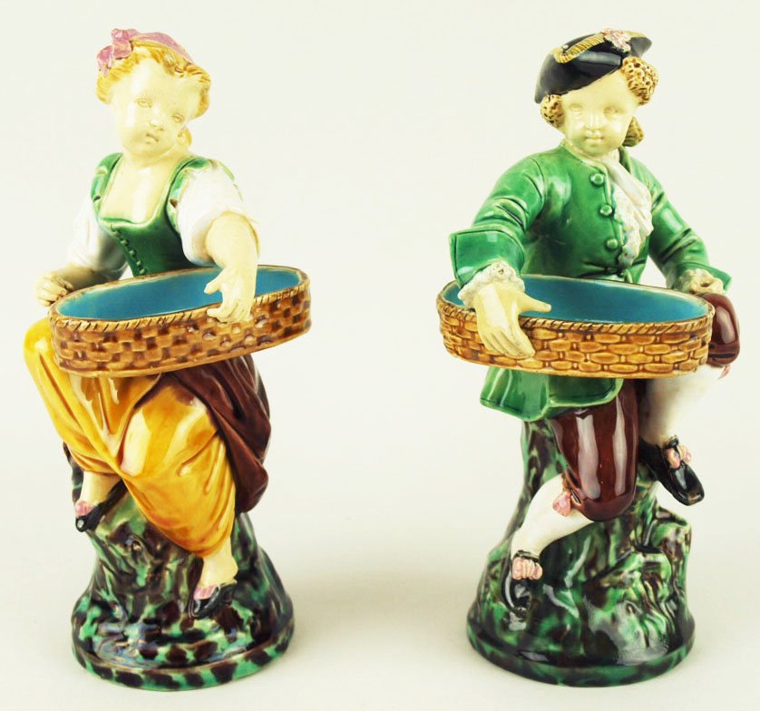 A fine pair of Minton Majolica ‘Hogarth Match boy’ and: A fine pair of Minton Majolica ‘Hogarth Match boy’ and Hogarth Match Girl’ c.1870 designed by Albert Carrier Bellouse, modeled as a boy and girl in 18th century costume, carrying imitation wicke