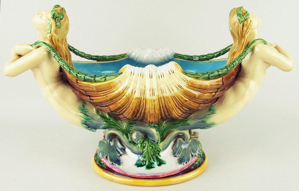 A Minton Majolica mermaid centrepiece c.1878, designed: A Minton Majolica mermaid centrepiece c.1878, designed by Carrier Belleuse as two mermaids supporting a large conch shell each holding a garland of acanthus, all supported on an oval base with a scall