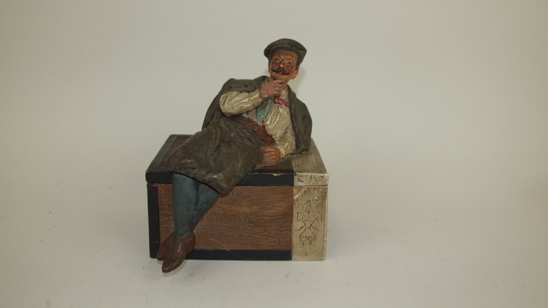 J.M. terra cotta figural humidor of man on cigar box,: J.M. terra cotta figural humidor of man on cigar box, repair to box