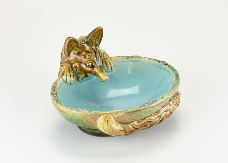 A George Jones Majolica ‘Fox’ Ashtray c.1875. Modelled: A George Jones Majolica ‘Fox’ Ashtray c.1875. Modelled as an oval bowl with a turquoise interior and a large fox peering over the side, clinging on with his front paws, his bushy tail curled aroun