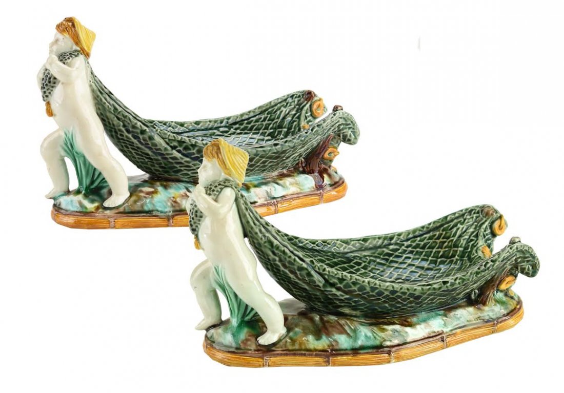 A Rare Pair of Wedgwood Majolica Net Jewel Stands: A Rare Pair of Wedgwood Majolica Net Jewel Stands c.1865. Each modeled as a putto dragging a fishing net, all on an oval rocky ground with an orange bordered pedestal base, 8”l, 5”h c.1865. Each m