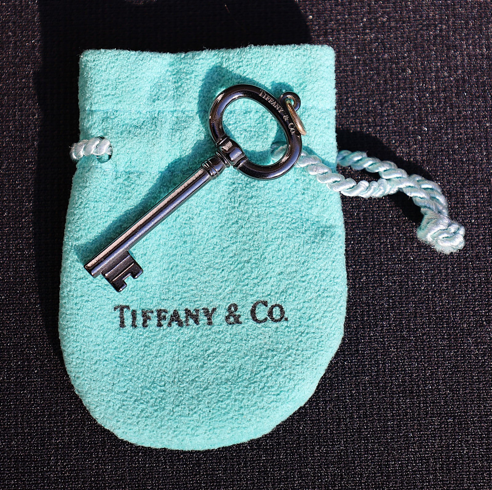 TIFFANY & CO, marked T & CO TI Black Titanium Key Pendant with Fabric Pouch. Size: key 1 3/4 in.: TIFFANY & CO, marked T & CO TI Black Titanium Key Pendant with Fabric Pouch. Size: key 1 3/4 in. x 3/4 in.
