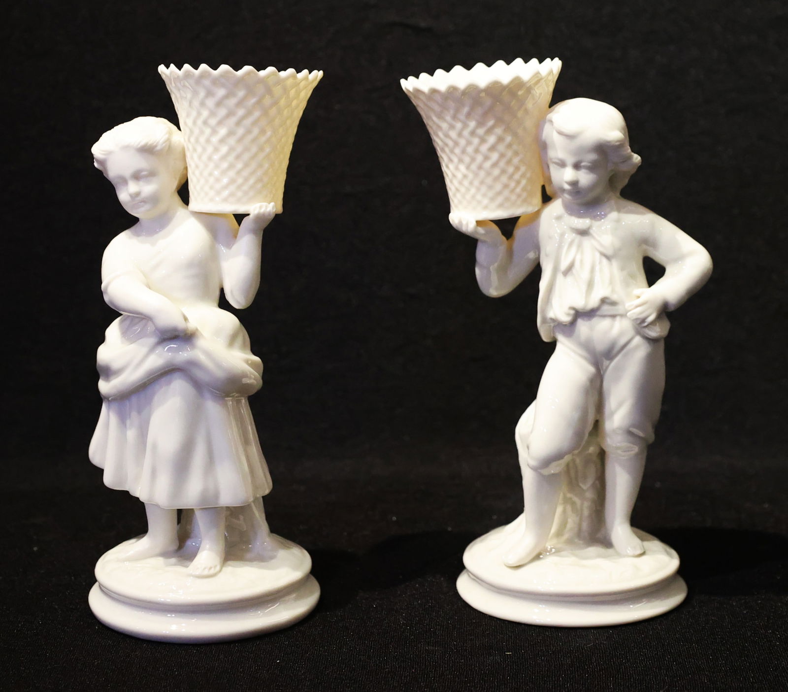 Pair Vintage Belleek Irish Porcelain Figural Victorian Boy And Girl Basket Holders. 8.5 In. Height: Pair Vintage Belleek Irish Porcelain Figural Victorian Boy And Girl Basket Holders. 8.5 In. Height; Size: 8 1/2 in. height x 3 1/2 in. wide