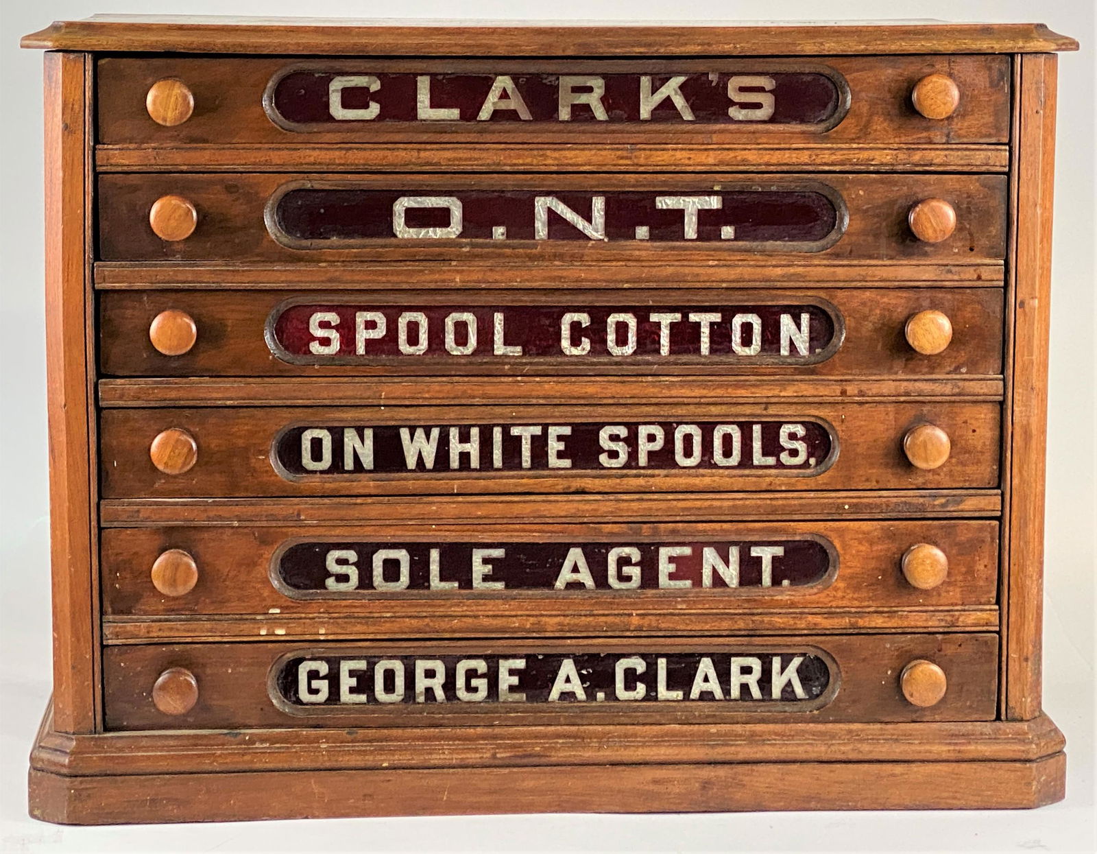 Clark's Spool Cabinet: A walnut, six-drawer spool cabinet with etched glass drawer labels promoting "George A. Clark's" Ontario-based company, ca. 1880, with wood-turned drawer pulls; 22" ht. x 29" wd. x 19" dp.
