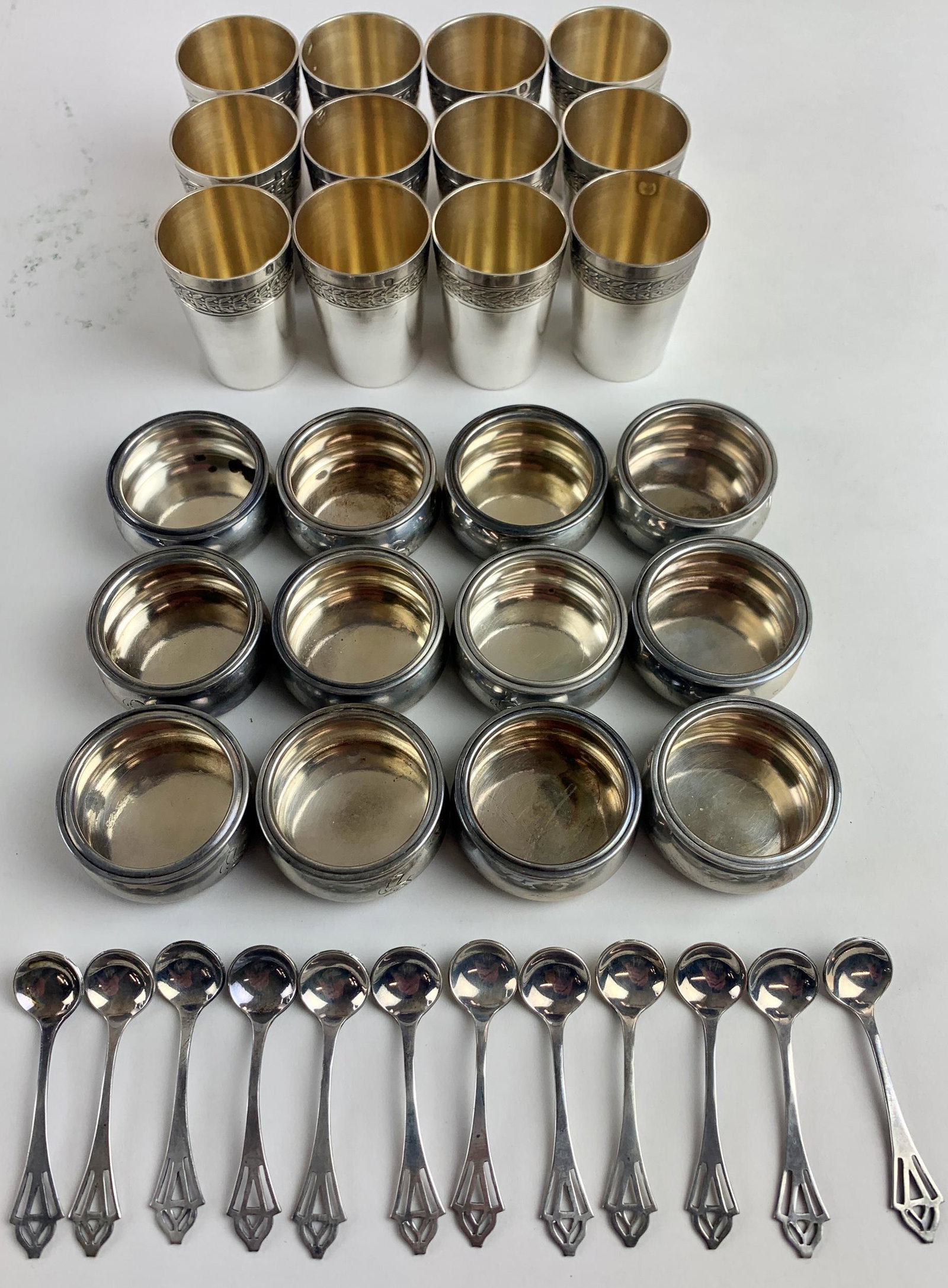 Collection of Sterling Salts, Spoons, and Glasses: A group of 12 sterling salts and sterling spoons, and also a group of 12 shot glasses, with several hallmarks to underside, exterior rim and interior (indistinct marks). Total weight 11.34 ozt. From t