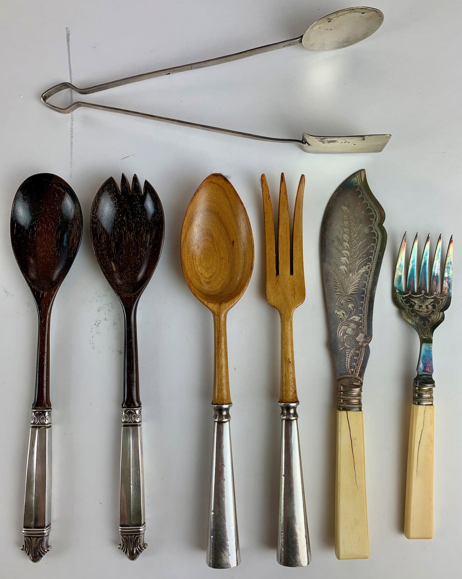 A Collection of Serving Flatware: A group of seven, including a Taxco Mexican sterling pair of tongs, as well as two pairs of wood pieces with handles, and finally an engraved pair with faux resin handles. Longest lg. 11". From the Es