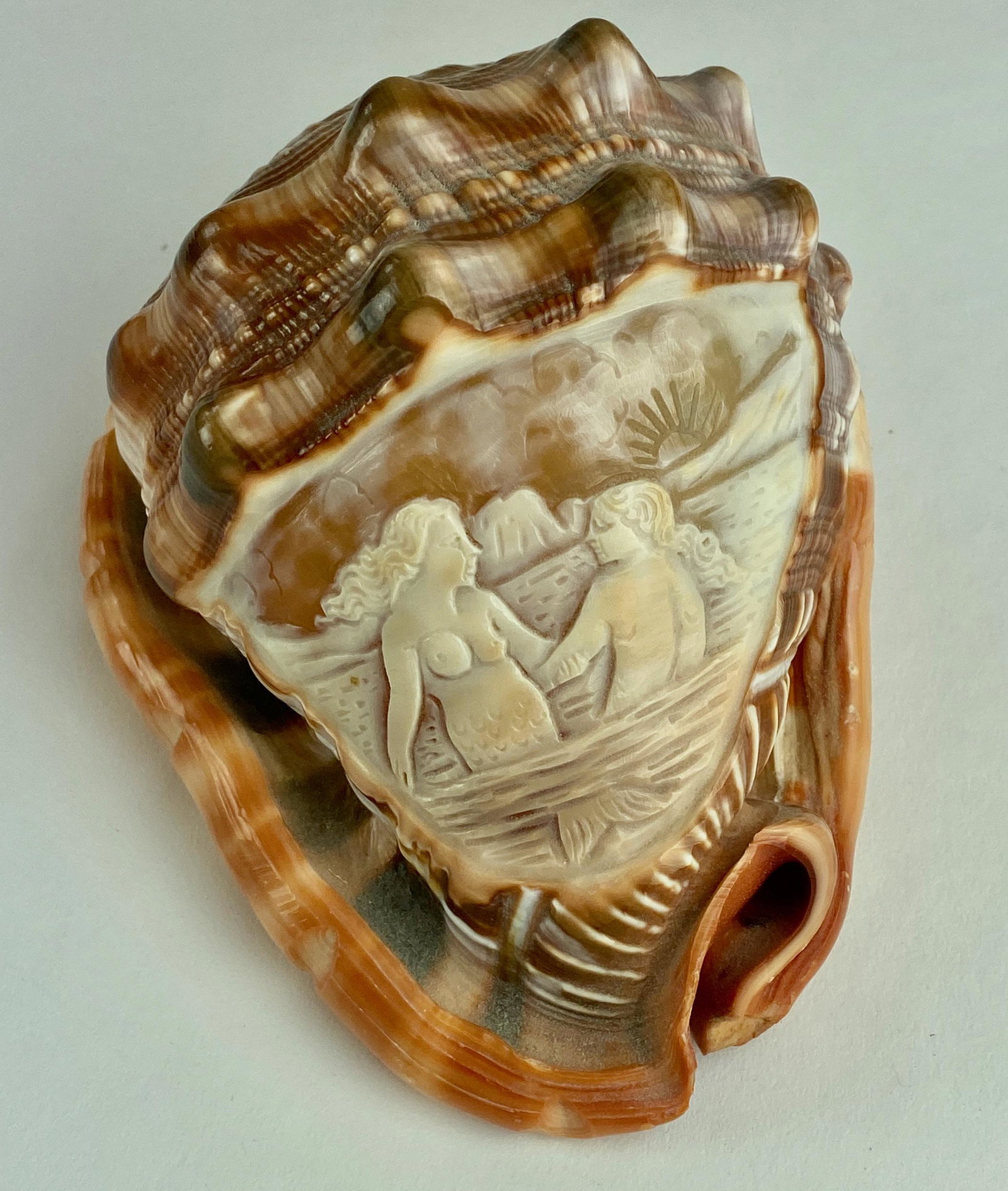 Hand Carved Conch Shell With Mermaids: A hand carved full conch shell, with reserve carved to reveal a pair of mermaids in a sunset; 6.25" x 4.25".