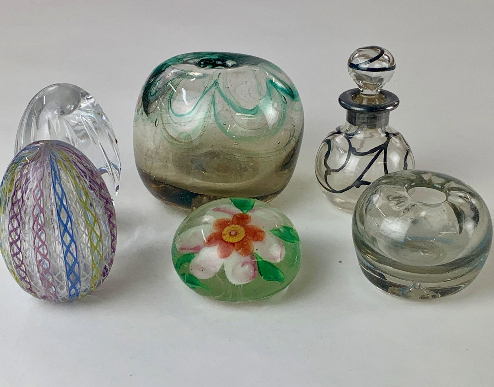 Grouping of Artglass and Crystal Paperweights: Six total paperweights, including an Atlantis crystal egg paperweight, two blown glass weights with holes to the top, and a floral puck-style example. Tallest 3.25" From the Estate of Harold and Miria