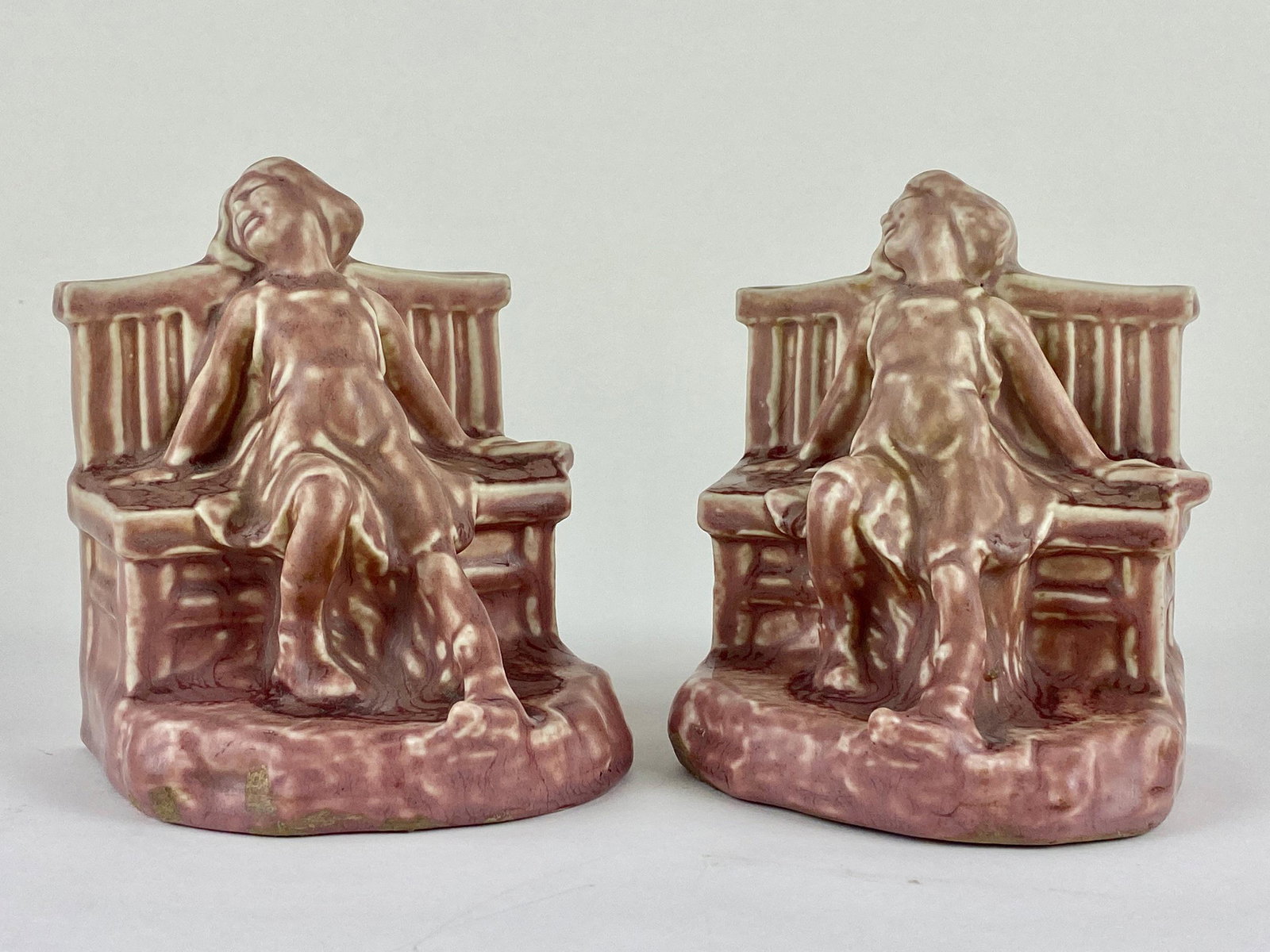 Pair of Rookwood Figural Bookends: Girl on bench bookend set by Rookwood Pottery, in cranberry matte glaze. Cast in 1924, with number 2446. Ht. of each 5.25" From the Estate of Harold and Miriam Prigozen, Dayton, OH.