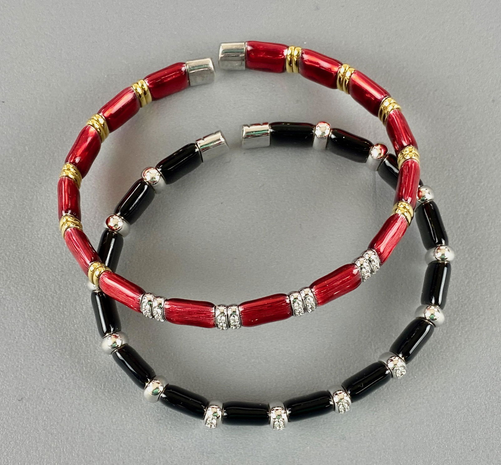 Pair of Henderson Collection Bangles by Lecil: One in red enamel with diamond and gold bars, and the other in black enamel with silver bars. Total weight: 47.8 grams From the collection of prominent art historian and lecturer, Robert Allen, New Yo