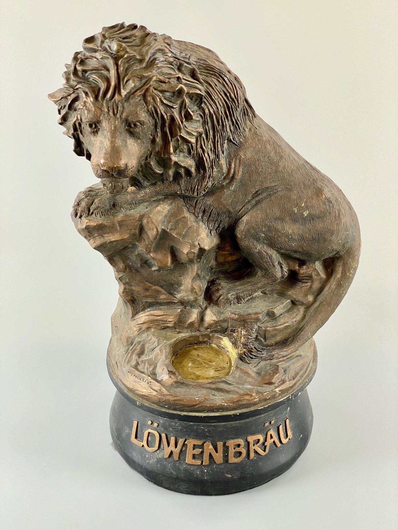 Lowenbrau Beer Advertising Lion Sculpture: A resin molded lion, gilt painted with the beer-maker's mark to the front reading "Lowenbrau." With a recessed rest for a beer bottle or pint glass and artist's engraved signature to the front. 18" ht
