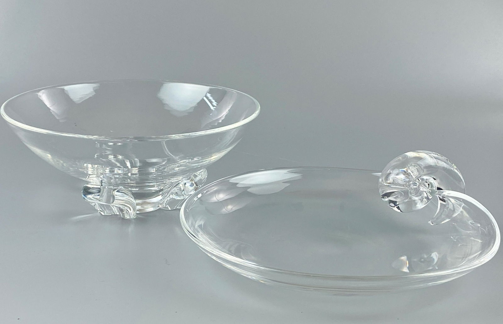 Pair of Steuben Glass Dishes: One with three-footed horseshoe design to base, the other a candy dish with snail design. Both in Steuben cloth carrying cases.