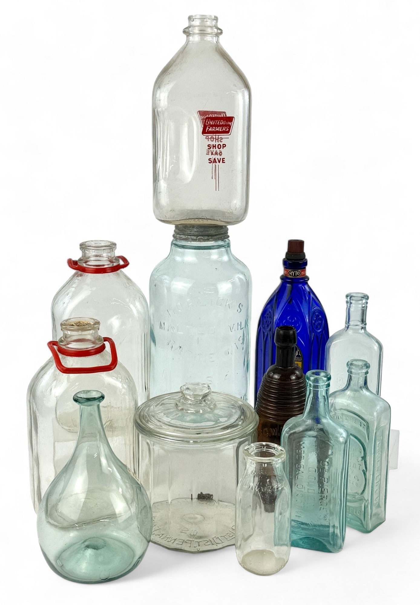 Collection of 12 Glass Bottles: Including a blown vessel, milk jugs, various medicinal remedies and more. Tallest height: 12"