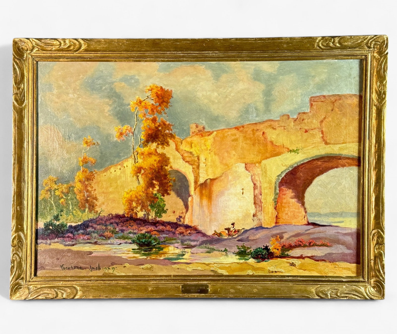 Theodore Jackman (1878-1940): American oil painting on canvas by Jackman, signed to the lower left. Housed in a nice gilt frame and depicting a cowboy atop horse riding through the western plains along a river under a bridge. Sigh