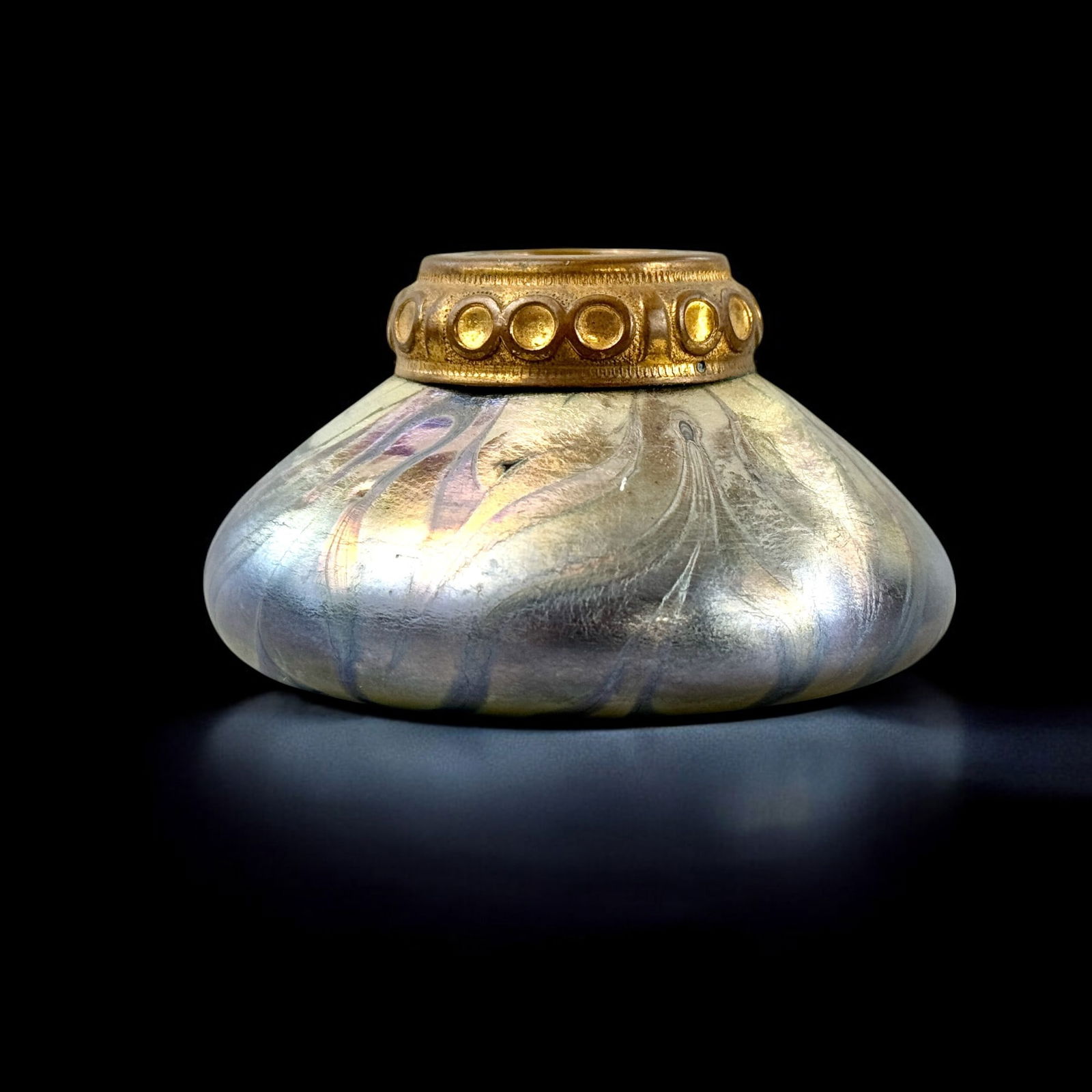 Irridescent Glass Inkwell with Ormolu Rim: Early 20th century, an iridescent Favrile glass inkwell with period brass ormolu rim. Ht. 1.75". Appears unmarked.