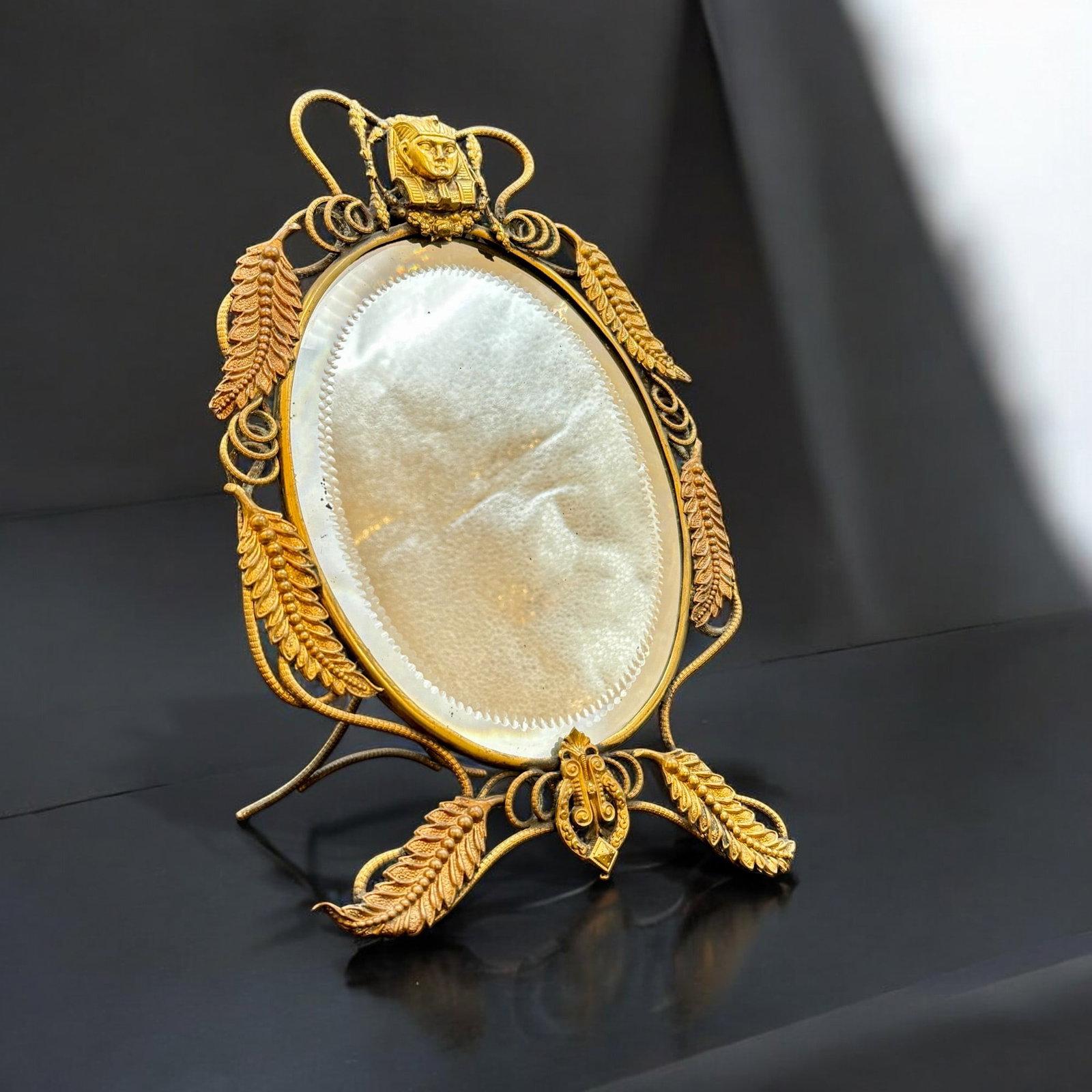 Egyptian Revival Ormolu Dressing Mirror: Late 19th century, an oval mirror with ormolu surround and perched pharoah, mirror with stipple design near border. Ht. 11.5". Property of an Illinois Collector.