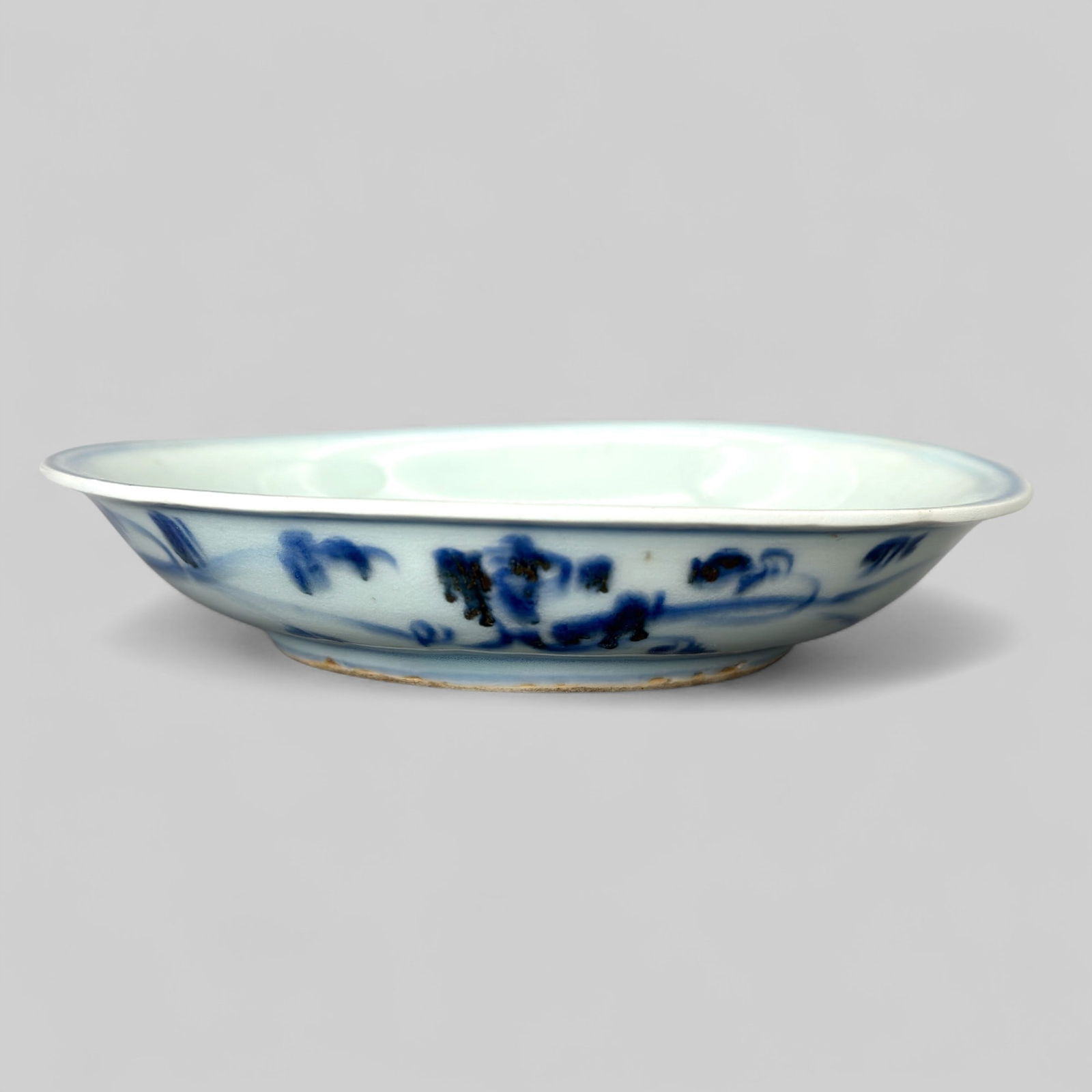 Porcelain Dish in Underglaze Blue, Ming, 16th Century: A dish with everted lip and rather thin, shallow foot is painted in a dark blue with a sketchy band of scrolled foliage on the underside. The inside has a galloping qiiin framed with various leaves an