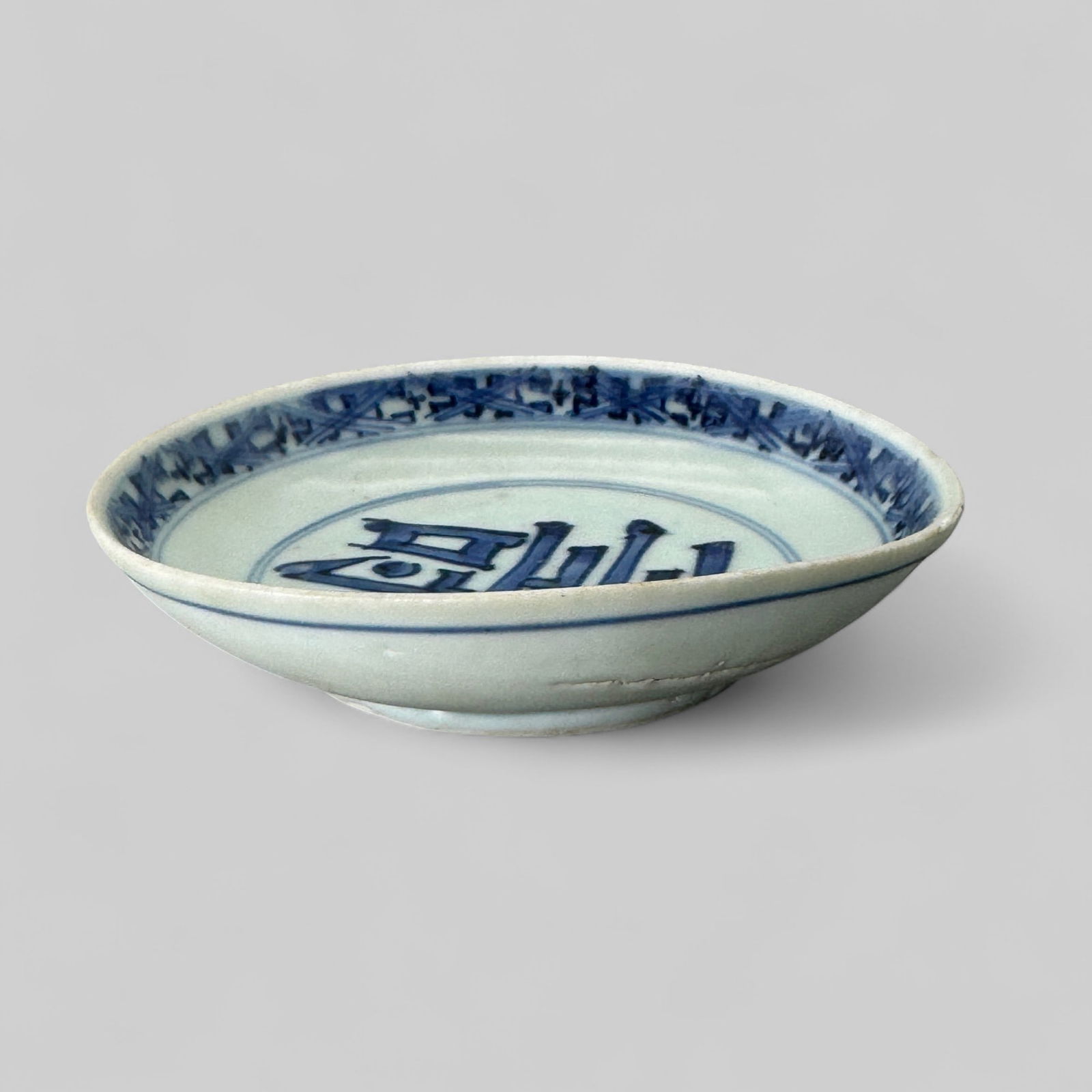 Porcelain Dish in Underglaze Blue, Ming: A small dish with rounded sides and a straight rim has a square seal mark on the base. The underside is undecorated; the inside has the character "shoo" (longevity) in the center and a diaper pattern