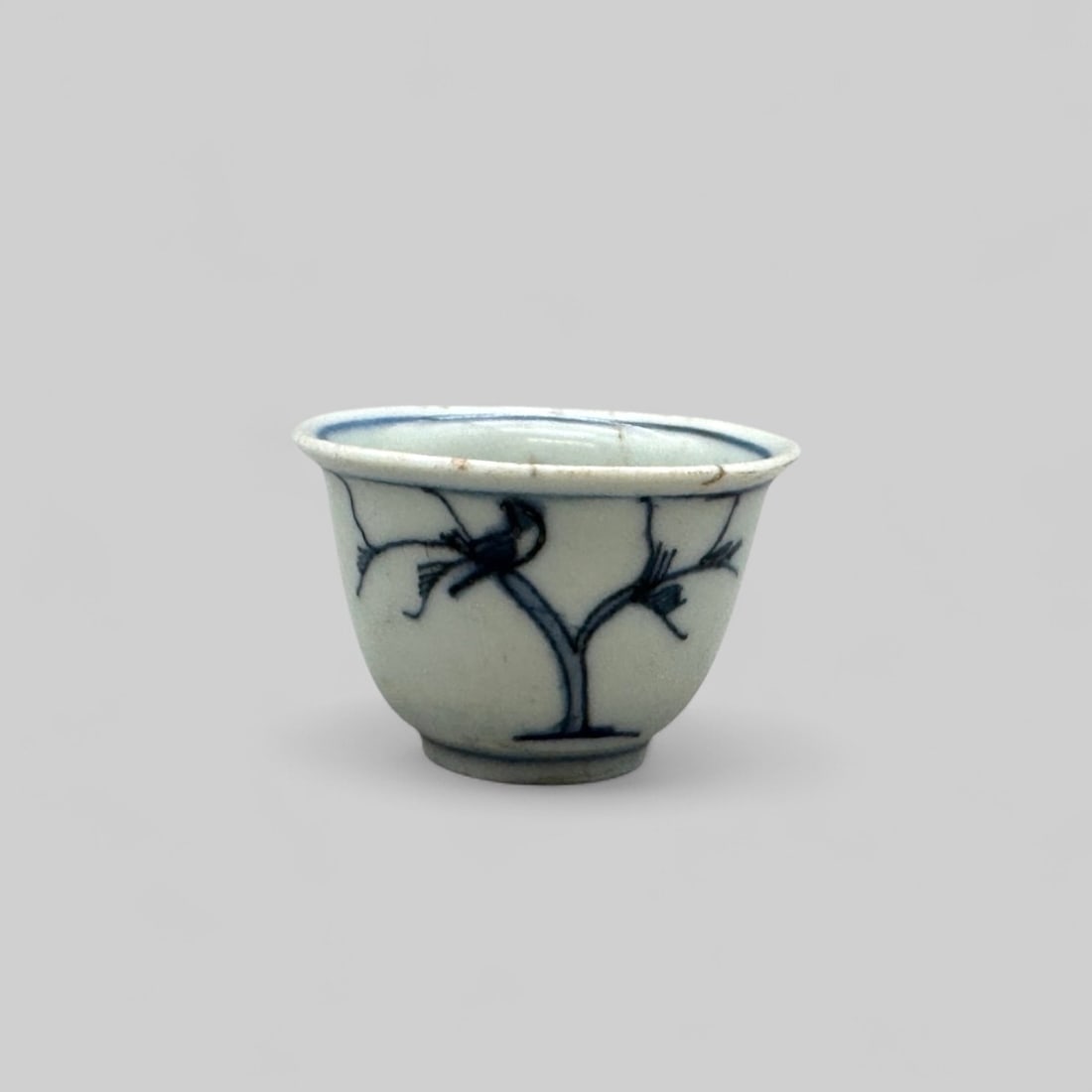 Porcelain Cup with Underglaze Blue, Ming, 17th Century: A cup with everted rim, thin foot, and unglazed base is painted with two trees, each with a bird on the left branch. Inside is a peach branch with a single fruit. Diameter 2.25" PROVENANCE