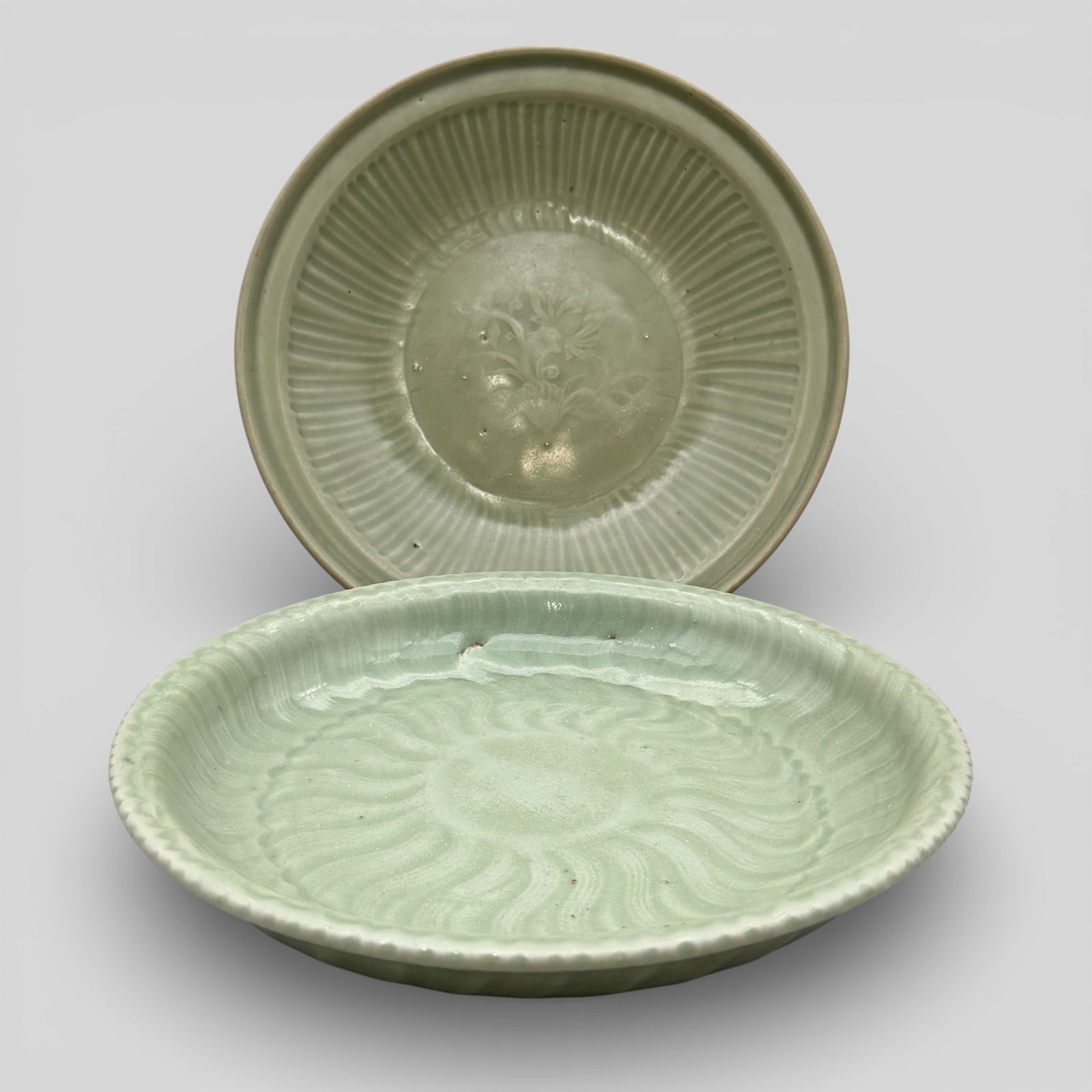 Pair of Large Longquan Celadon Shallow Chargers: Song/Yuan dynasty. One with scalloped rim and sunburst decoration carved to interior, the other with bouquet of flowers and lobing to interior. One in a deeper sea green glaze than the other. Both wit
