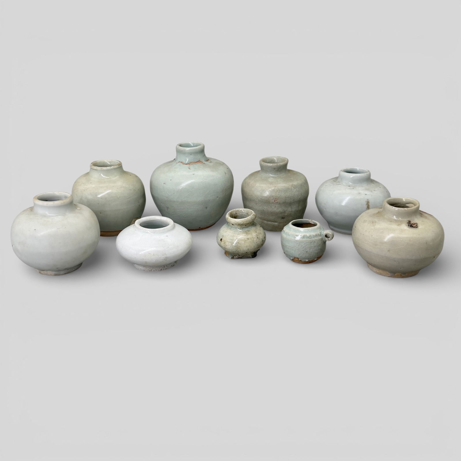 Group of 9 Song/Yuan Celadon Jars: All in varying shades of celadon glaze, six of them with heavy crazing. One pure white example. One with label to side. All with unglazed feet. Tallest height: 3 1/8" PROVENANCE