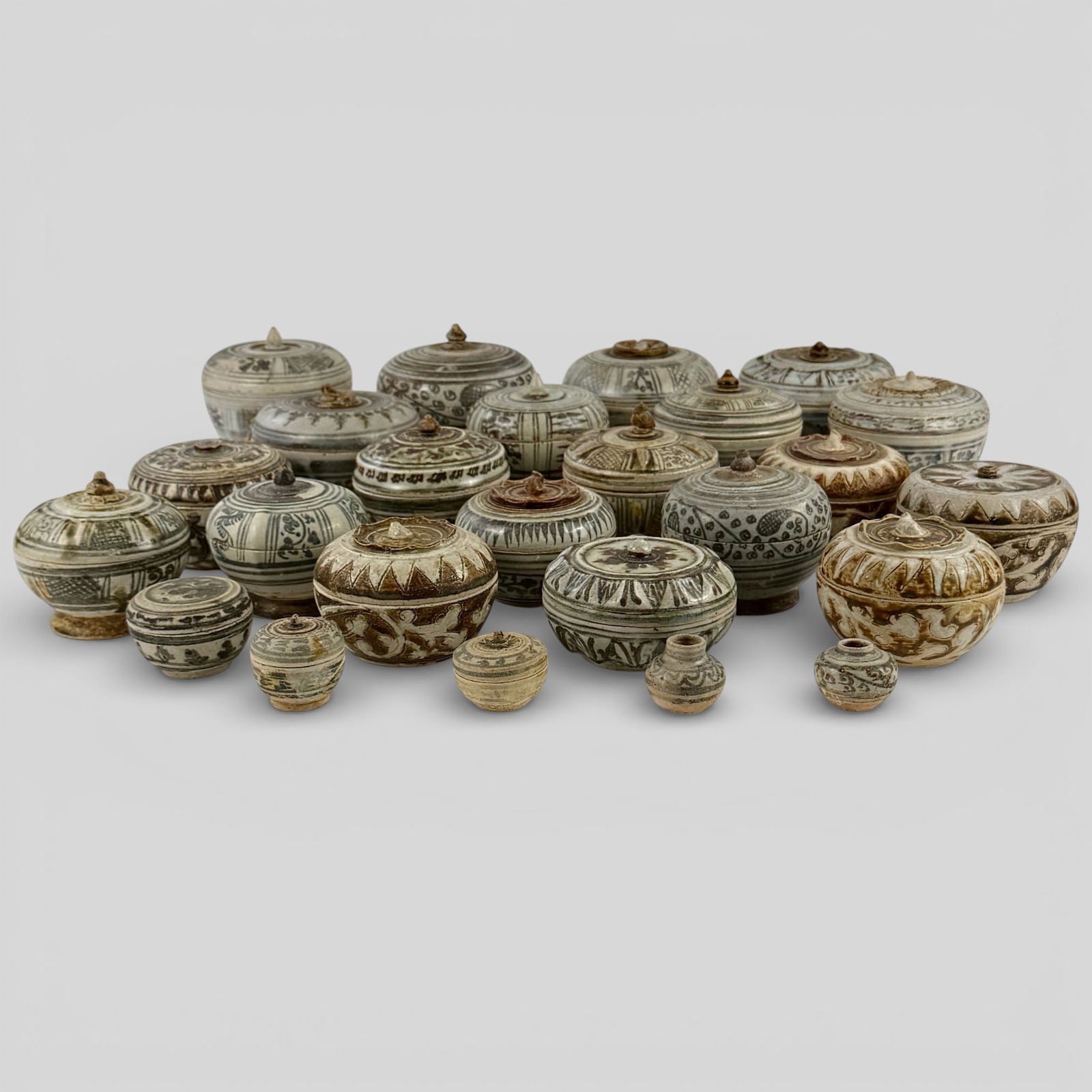 Huge Collection of Annamese Covered Jars: 23 jars in total, all with either underglaze blue or brown decoration. All fully decorated, carved. Many with geometric patterns. Some with finials. Some finials pointed. Unglazed foot to each. Some s