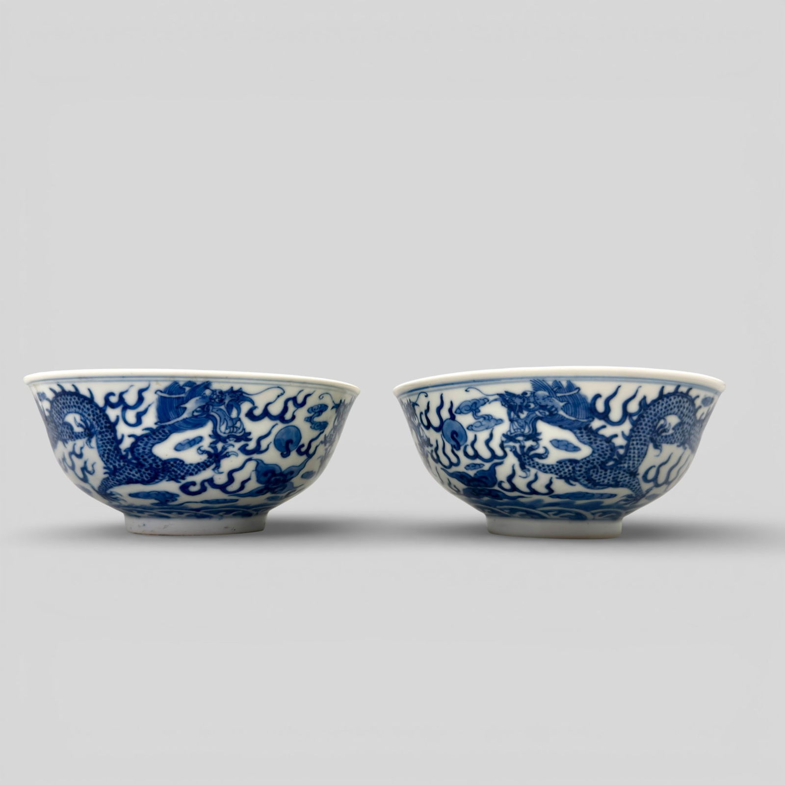 Pair of Qing Dynasty Blue and White Dragon Bowls: A pair of small blue and white porcelain bowls, decorated in underglaze blue. Each in comparable decoration, with dragon chasing the flaming pearl, waves and double ring near the foot. Each bowl with