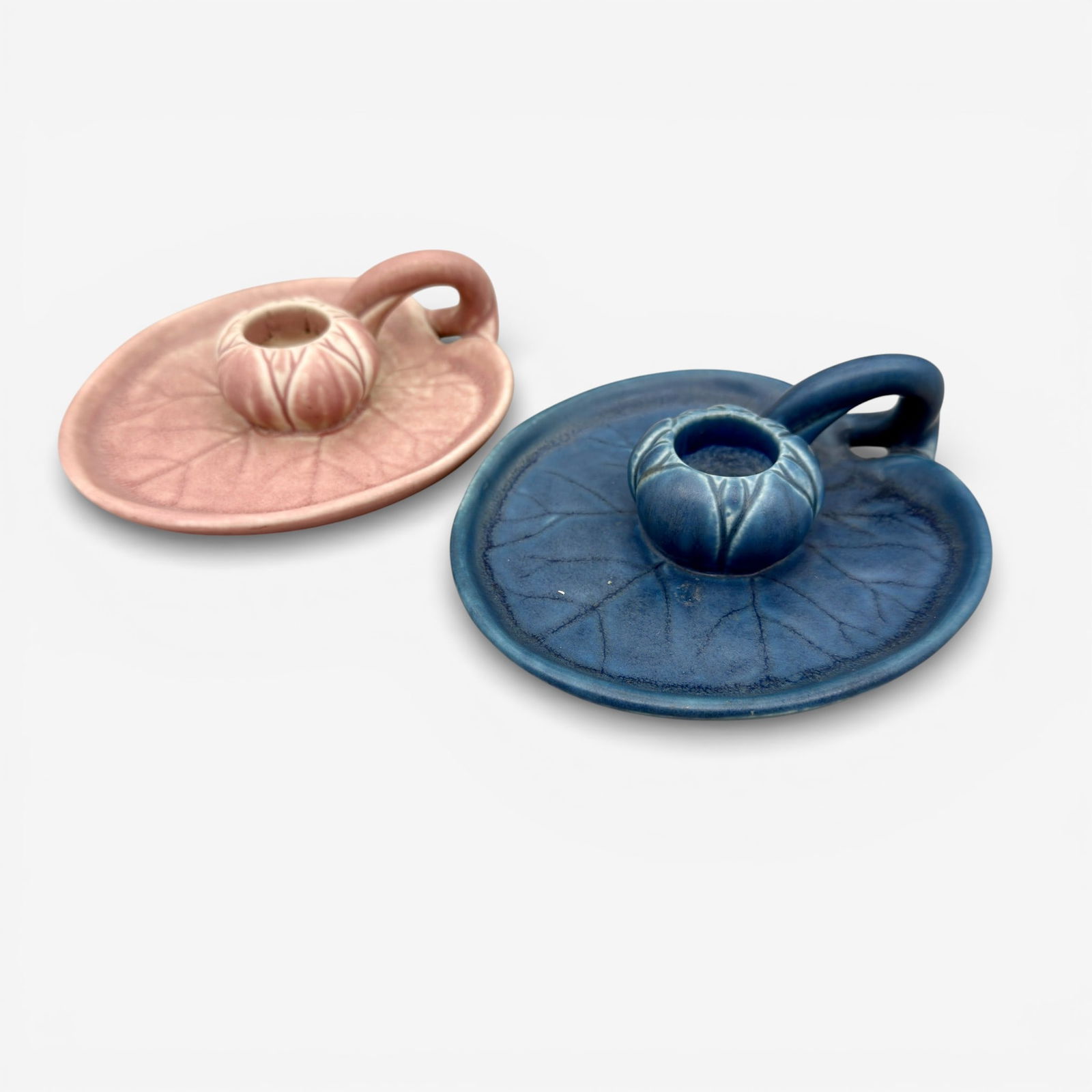 Group of two Rookwood candleholders,1923 and 1930: Two Rookwood candleholders, one pink, the other blue. Impressed Rookwood logo, XXIII and XXX, Shape numbers 1067. Height 1 1/2 inches. Width 5 3/8 inches.