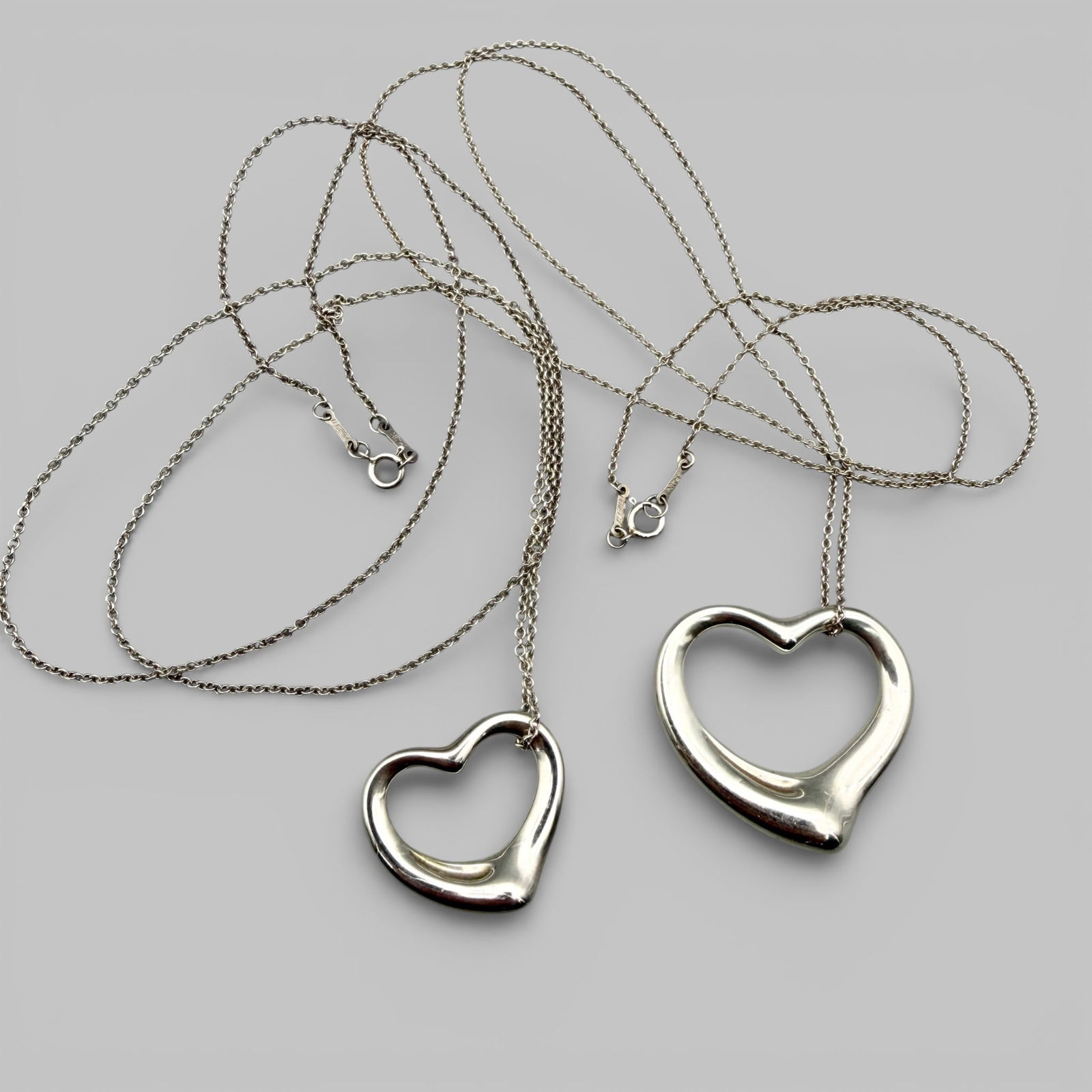 Pair of Tiffany and Co. Elsa Peretti Sterling Heart Necklaces: In original bags. Both in sterling silver and both stamped with Tiffany and Co., Elsa Peretti, 925 silver. Weight: .96 troy ounce