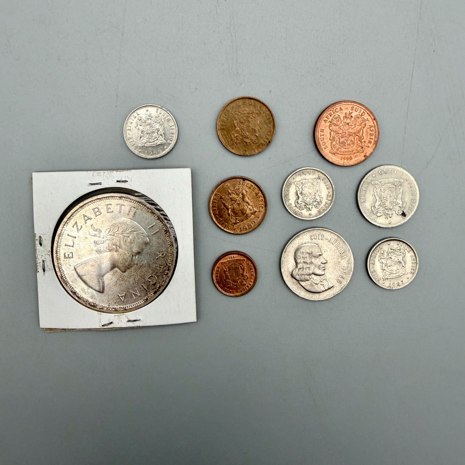 Group of South African Apartheid and Silver Coins: Includes Elizabeth II silver 5 Shilling (1955 BU) and nine South African Apartheid-era coins from the 1960sâ 1990.