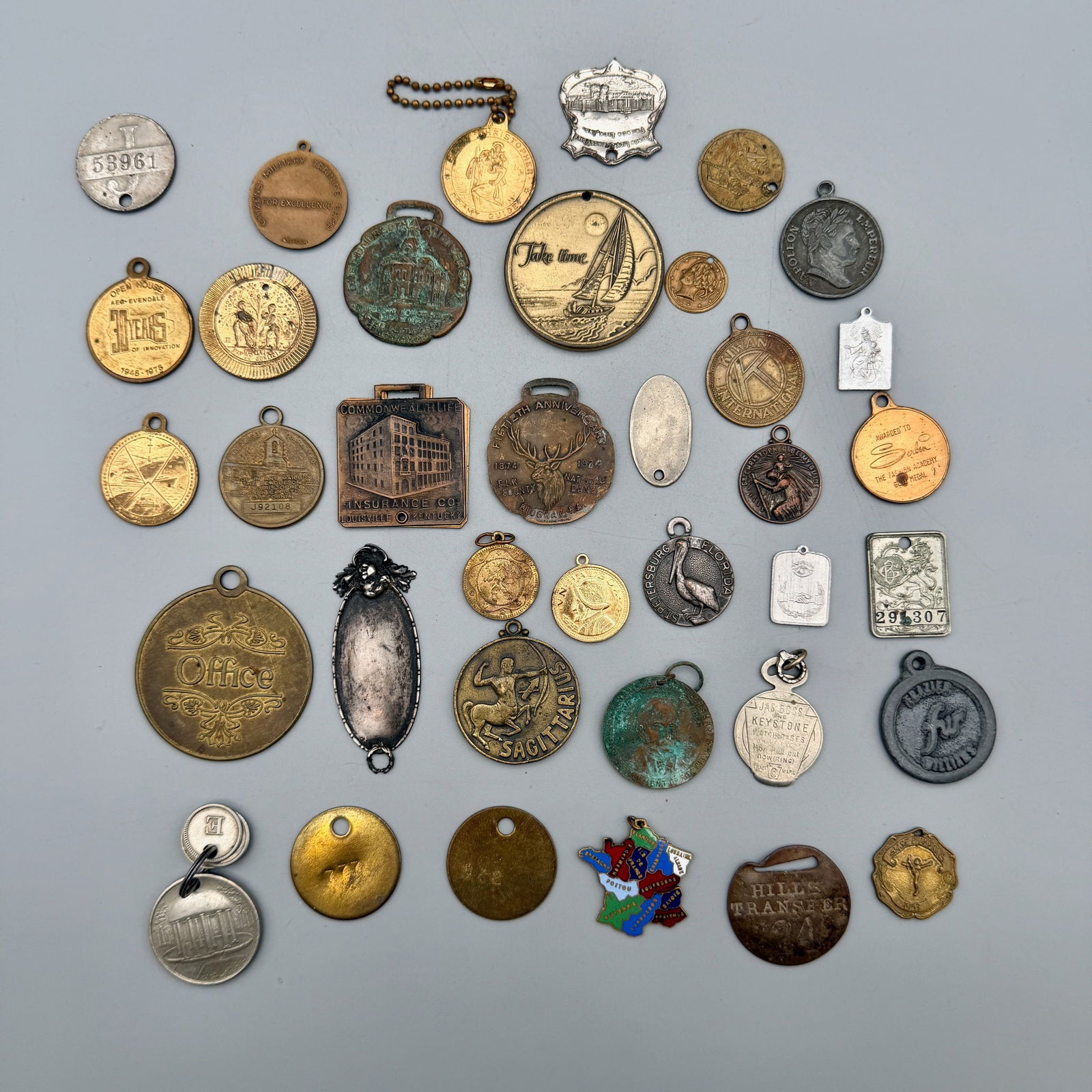 Thirty-Seven Watch Fobs & Key Chain Medallions, 19th-20th Centuries: 37 mixed bronze, brass, nickel, aluminum, sterling, plated and enameled fobs including Elk County; Commonwealth Life; St. Christopher; Kiwanis; Napoleon; French Lick Springs; Greenbrier; Cyrus Stall;