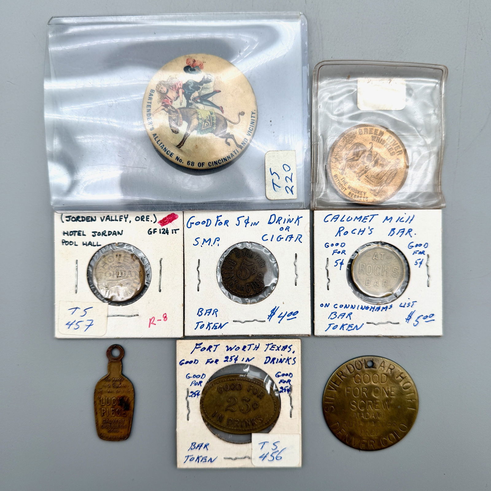 Group of Alcohol Related Tokens, Fobs, and Pins: Includes 1898 Lincoln Freedmen’s Aid cello pinback; Calumet MI saloon; Denver Silver Dollar Hotel brothel token; George’s Gateway Rendezvous; Jorden Valley OR; early western saloon; Green River Wh
