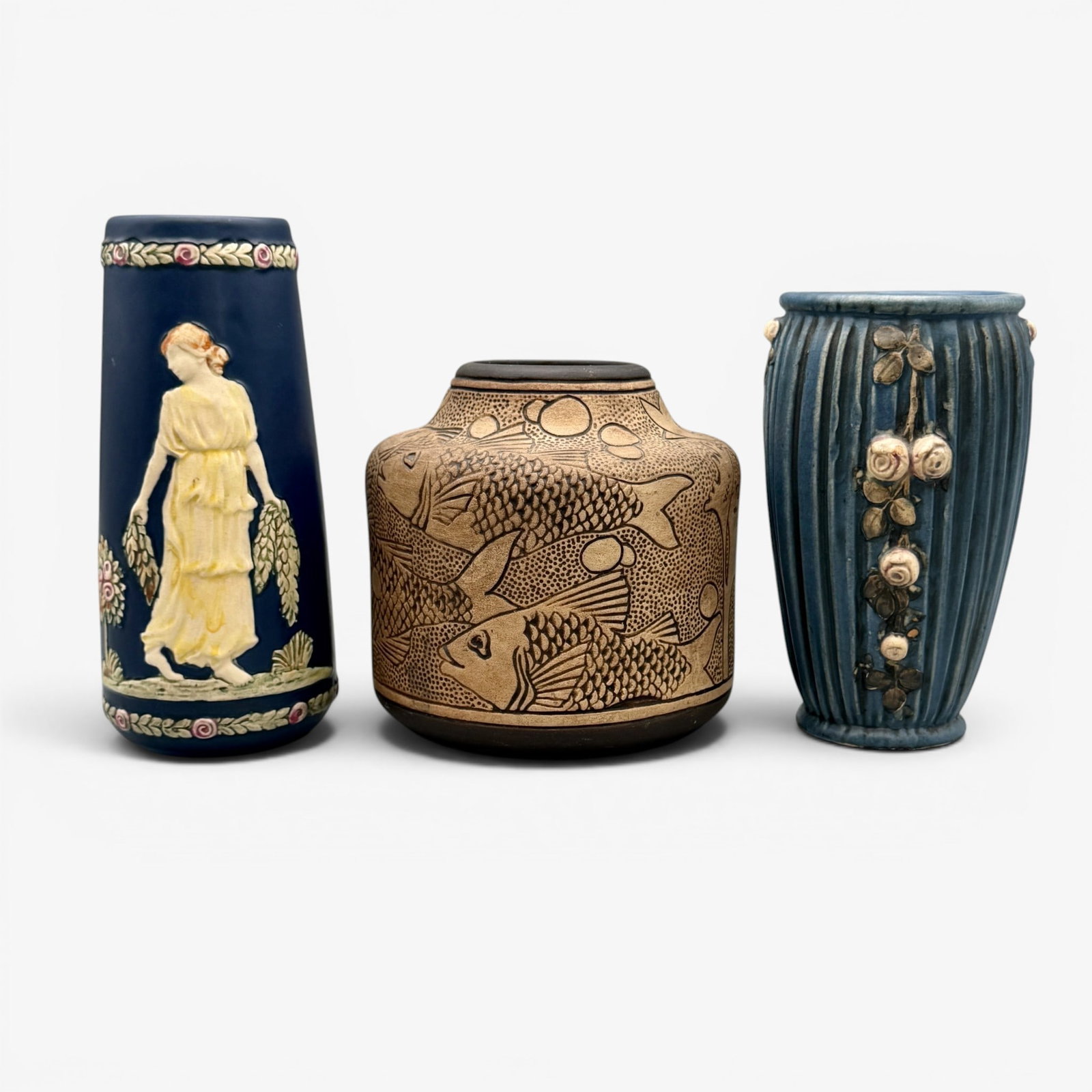 Group of Weller Pottery. Blue Ware, Blue Drapery and Burntwood.: Three Weller items. Burntwood vase with fish, Blue Drapery floral vase and Blue Ware vase with dancing maidens. Height of tallest, 7 3/8 inches.
