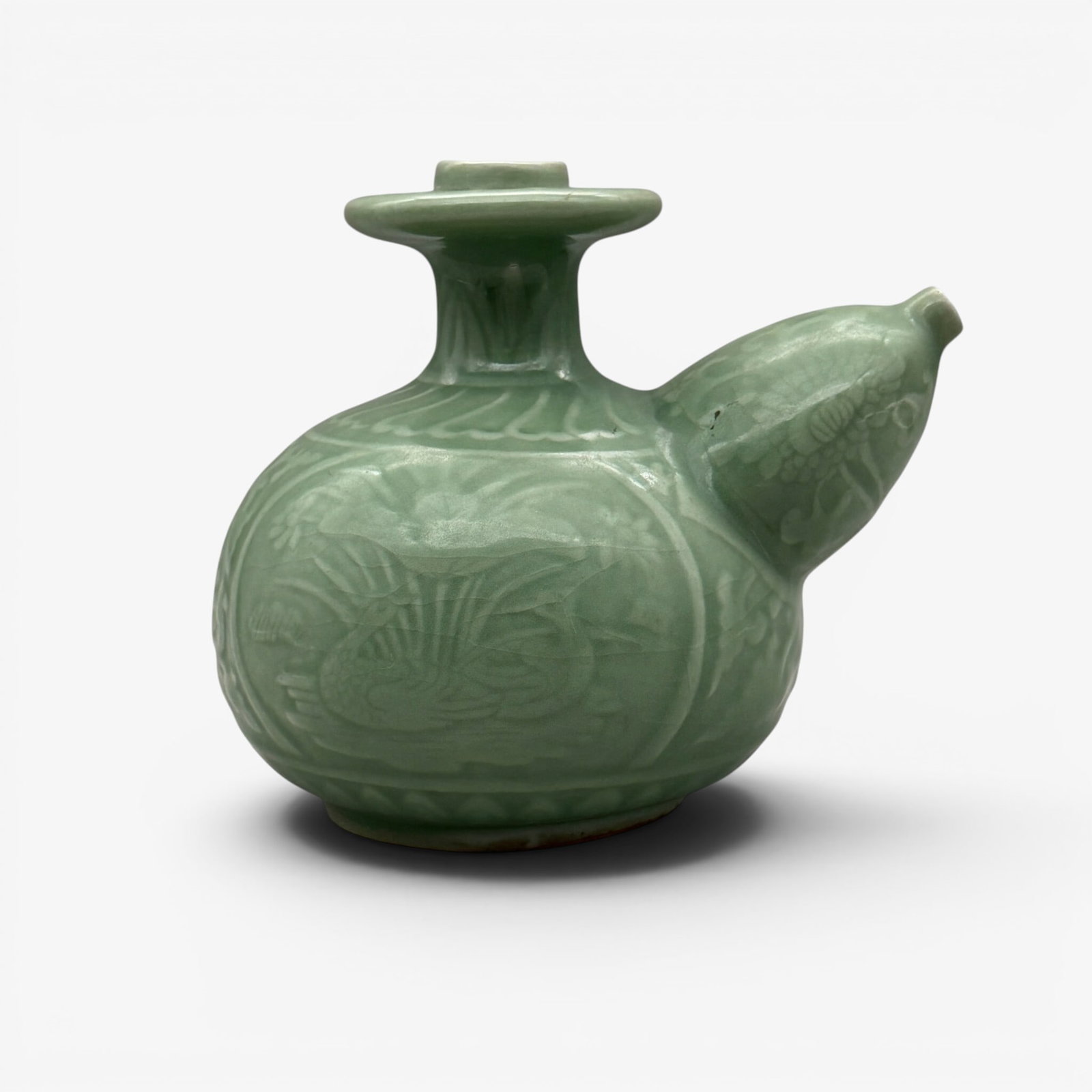 Carved Longquan Celadon Kendi: Song/Yuan dynasty. Intricately carved with pairs of geese sitting in water to both sides. Flowering blossoms extend north from the geese. Floral decoration to the spout. Leaves to rim. Unglazed foot.