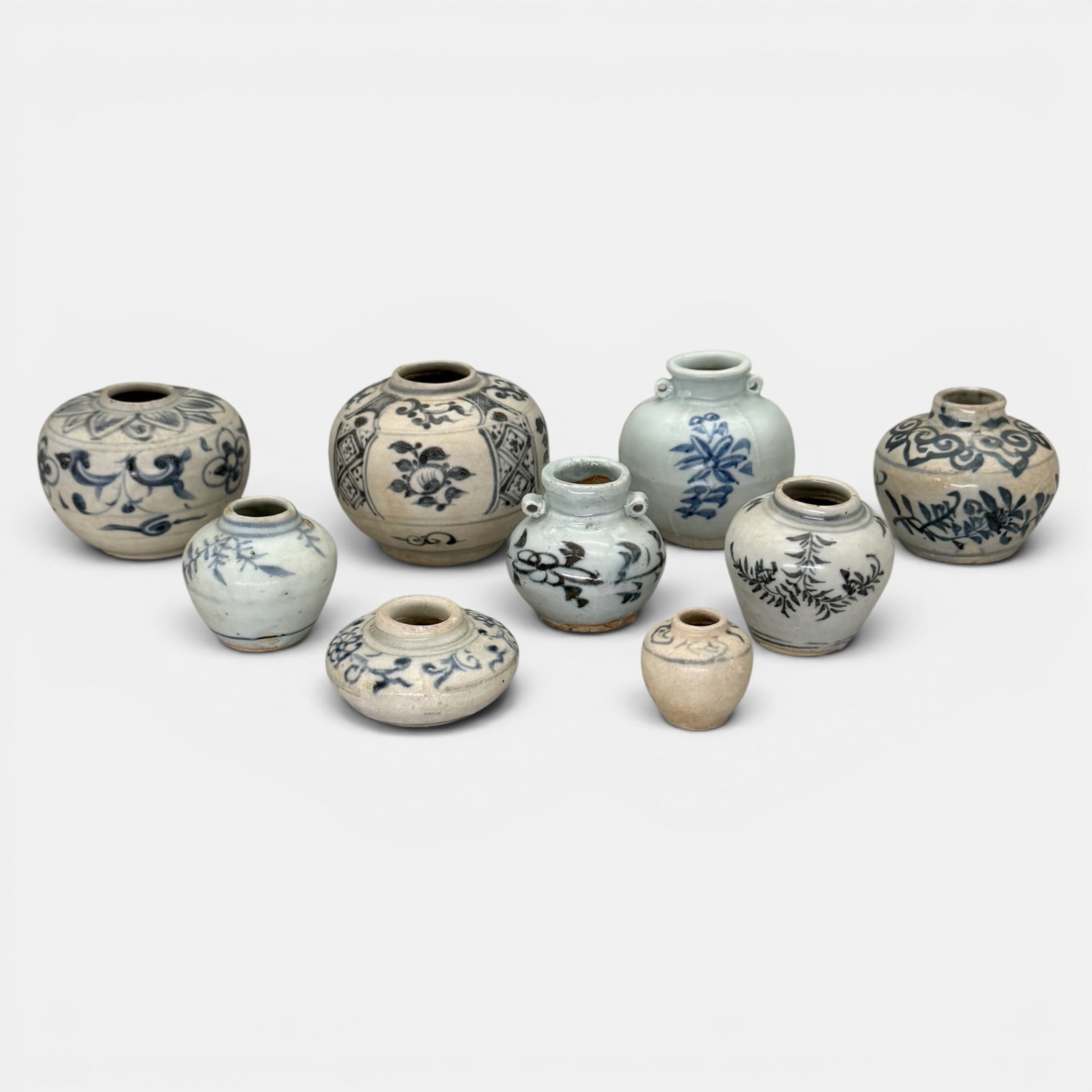 Blue and White Jarlets, Yuan: Yuan dynasty, a nice collection of nine small jars, including one shallow ink jar or washer, most with leafy or floral blue underglaze to exteriors. Tallest ht. 3".