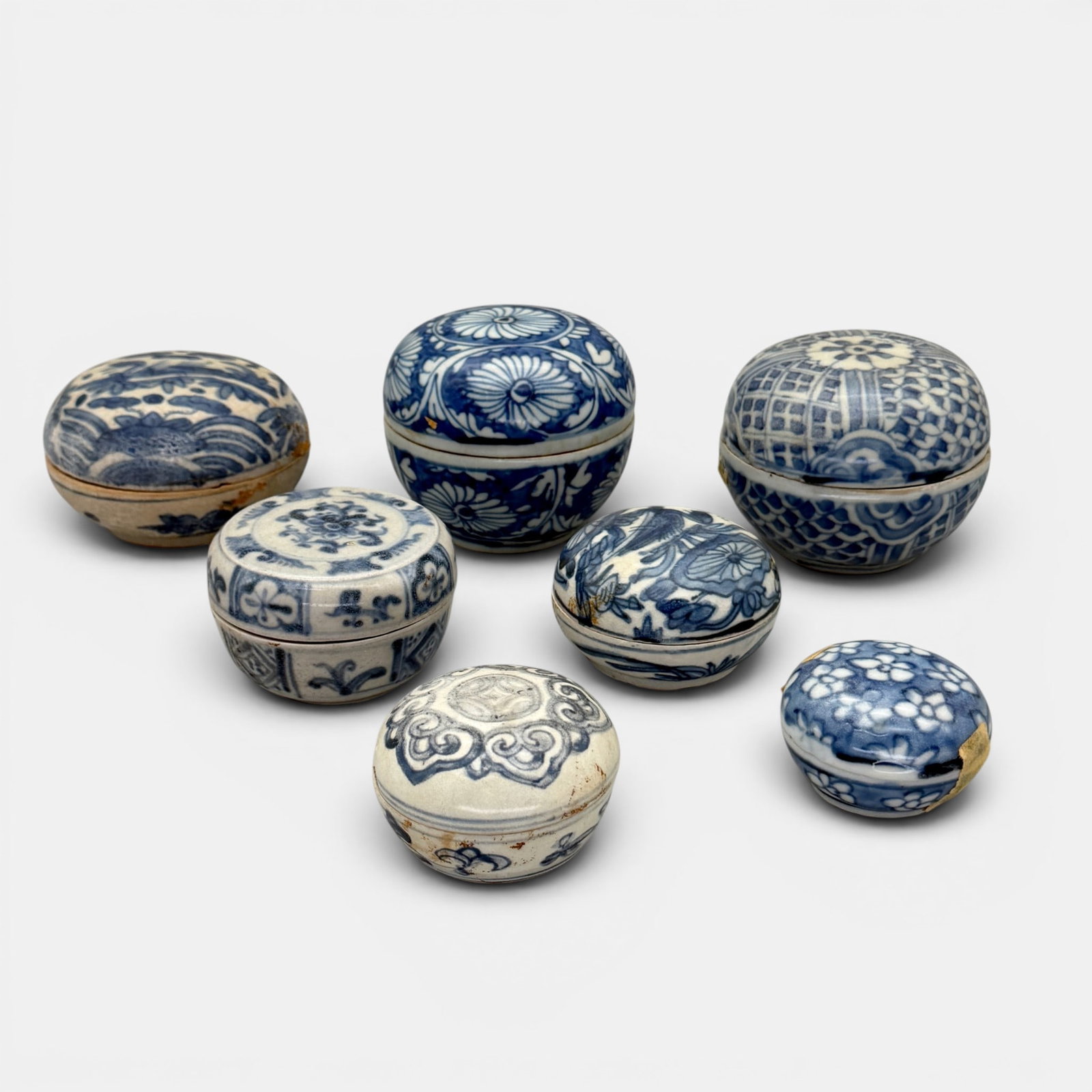 Group of 7 Ming Blue and White Covered Boxes: Some with floral design, some with cranes. One box with significant crazing and glaze loss, others with crazing as well. Largest diameter: 3.75", tallest height: 3.25"