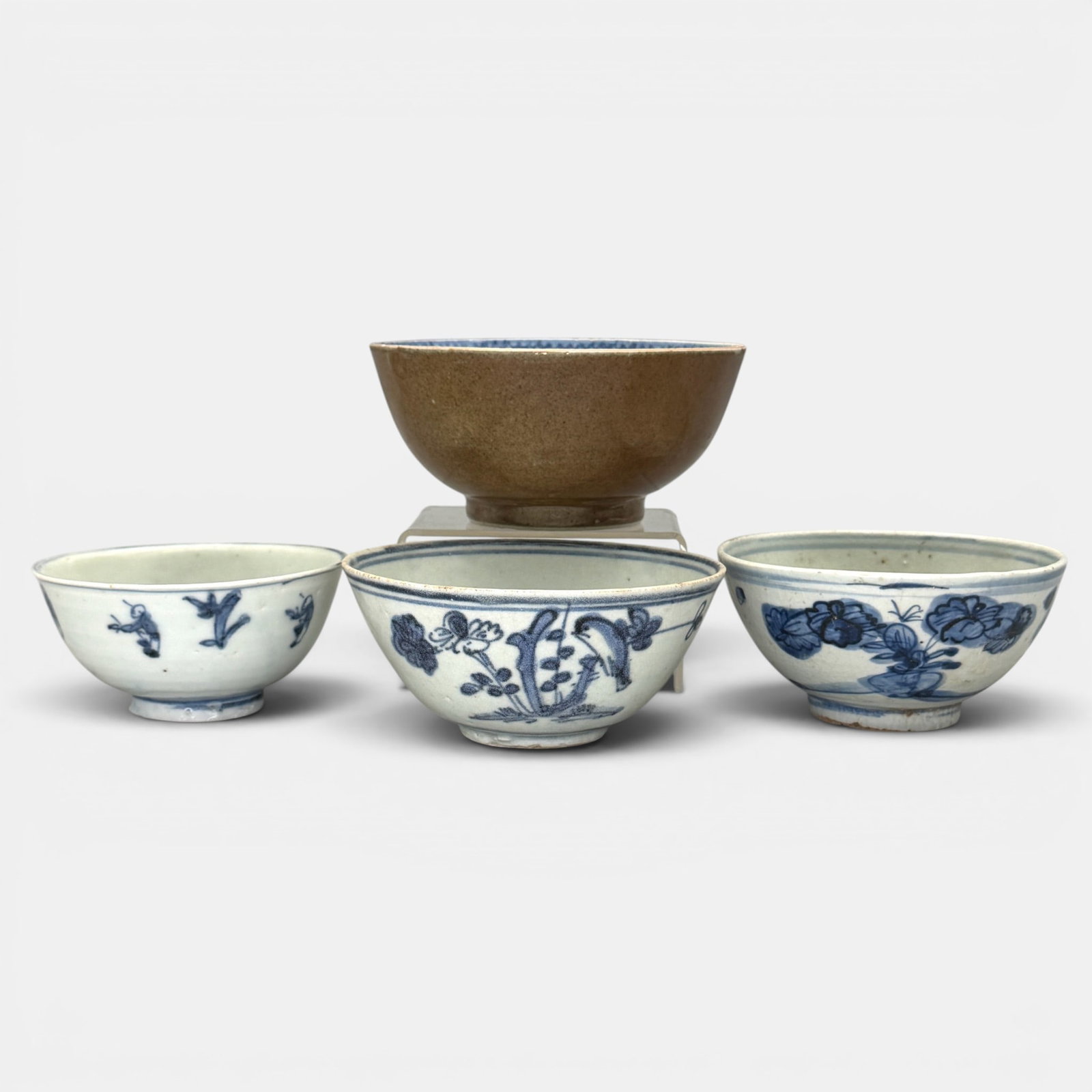 Four Early Chinese Bowls, Ming: Three Ming blue and white decorated floral designed bowls, and one additional bowl with interior decoration a deep brown glaze to exterior