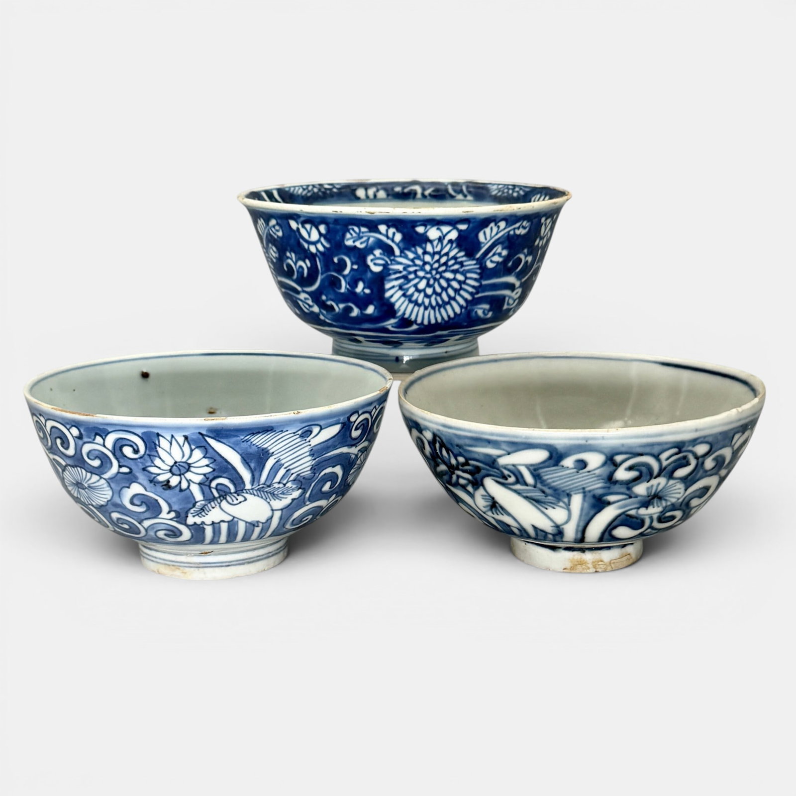 Three Underglaze Blue Ming Bowls: Each with blue ground, one with peonies in white over a heavy blue ground, double ring and dual fish mark to underside. The others in bird and floral splay decoration. Largest ht. 3", diameter 6".