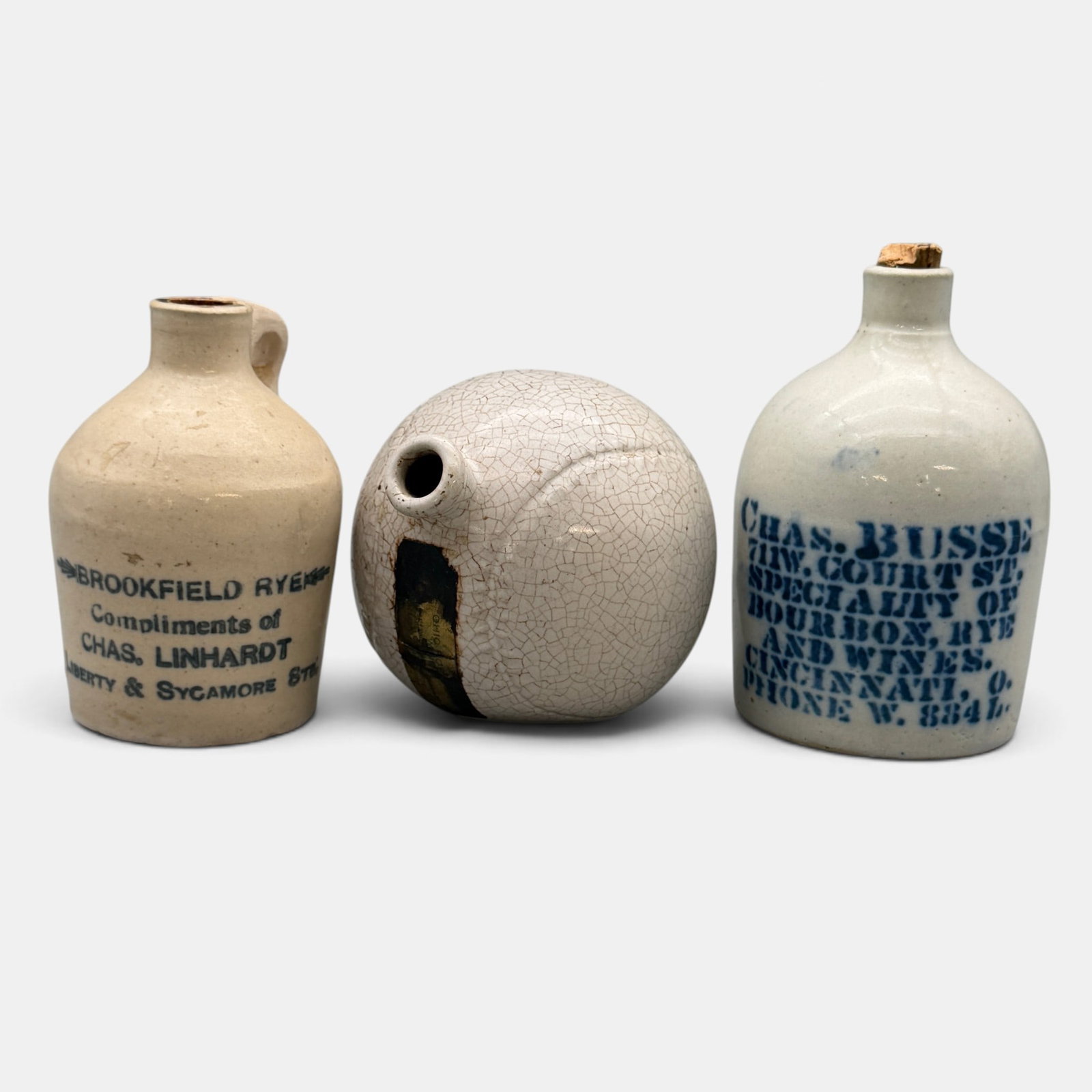 Three small whiskey jugs, Chars. Busse, Cincinnati, Charles Linhardt, Cincinnati and a baseball: Three small whiskey jugs. 1. Chas. Busse 711 W Court St. Speciality of Bourbon, Rye and Wines. Cincinnati, O. Phone W. 884 L". Height 4 1/2 inches. 2. Brookfield Rye, Compliments of Chas. Linhardt, Li
