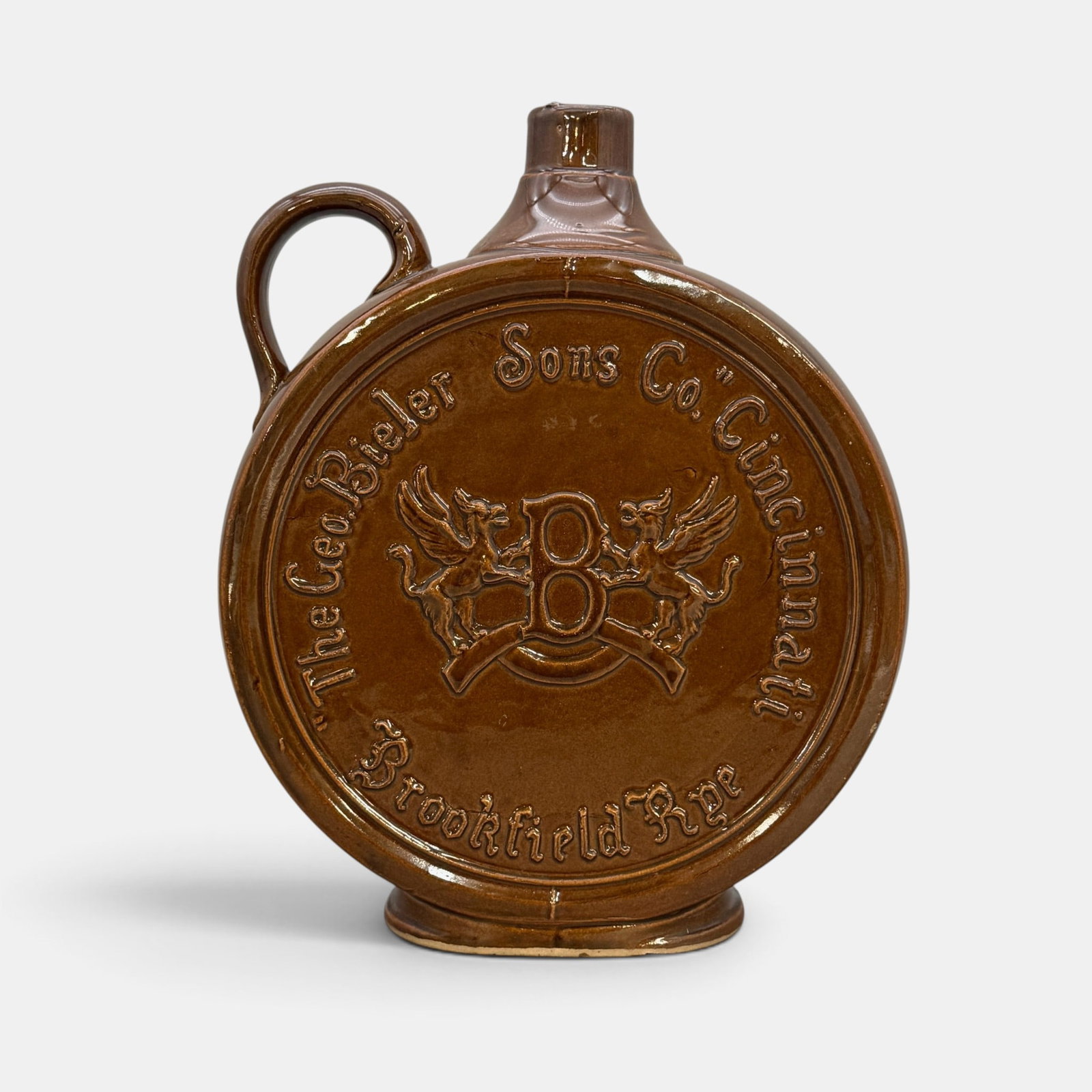 George Bieler Sons, Cincinnati , Brookfield Rye jug: A nicely glazed George Bieler Sons, Cincinnati flat sided pottery Brookfield Rye ju g having two winged creatures flanking the letter B in the center. Height: 12 1/2 inches. From the Jerry Stehlin Col
