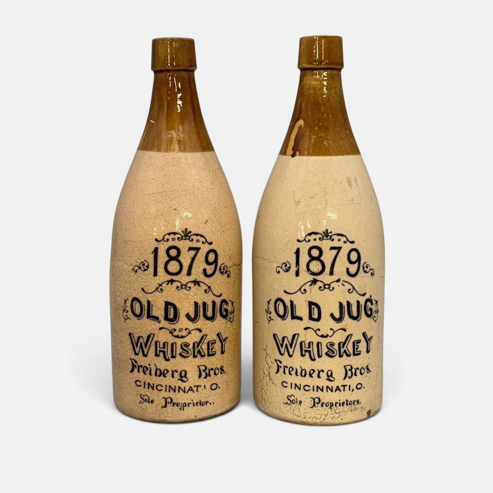 2 Freiberg Brothers whiskey bottles, Cincinnati,: 2 Freiberg Brothers ceramic 1879 Old Jug Whiskey bottles. Both lithographed "1879 Old Jug Whiskey Freiberg Bros. Cincinnati. O. Sole Proprietors." Height of each is 10 3/4 inches.