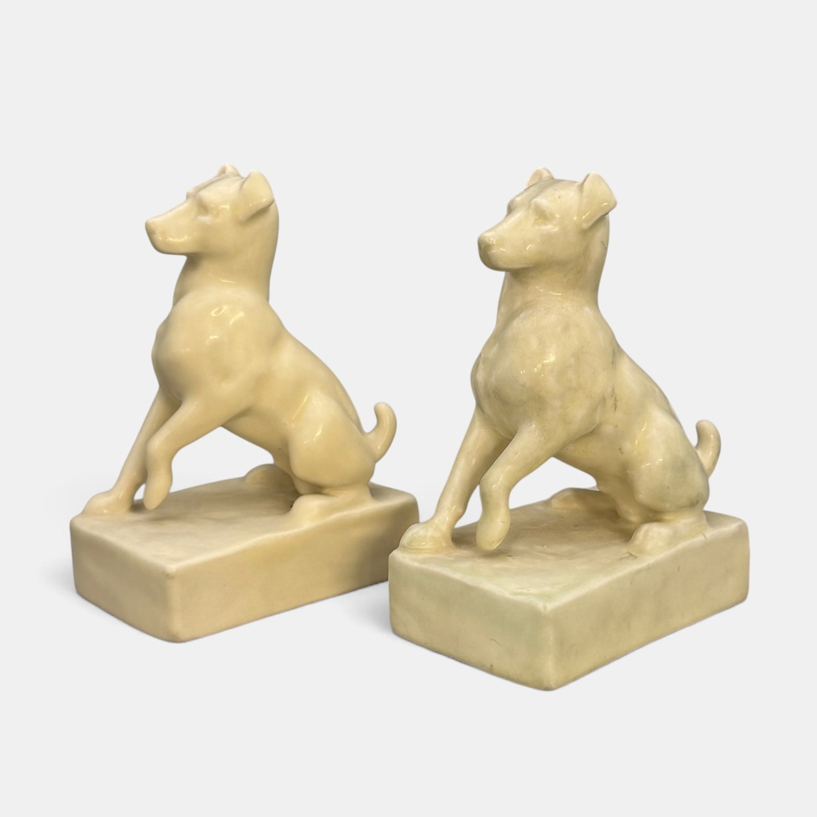 Two Rookwood "Dog with lifted Paw" paperweights, 1924 and 1932.: Two Rookwood "Dog with Lifted Paw" paperweights in white mat glaze, a William McDonald design. Impressed Rookwood logo, XXIV and XXXI. Shape number 2777. Height of each is 4 7/8 inches.