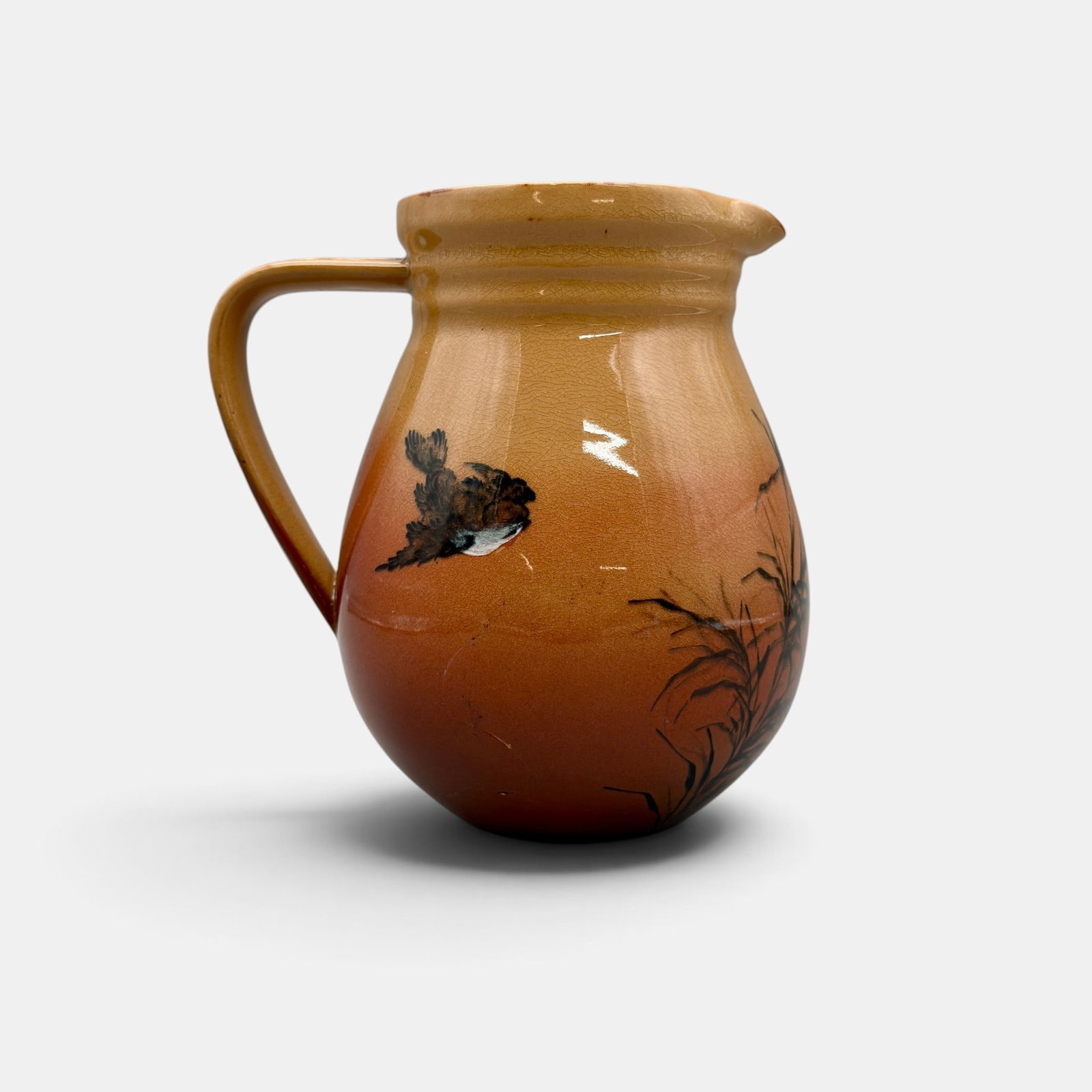 Rookwood Limoges style pitcher, sparrow, AMB, 1886: Rookwood Limoges style pitcher featuring a single small bird in flight amidst Asian grasses. Done by Anna (Bookprinter) Valentien in 1886. Impressed ROOKWOOD 1886, Shape number 54 B, G for ginger