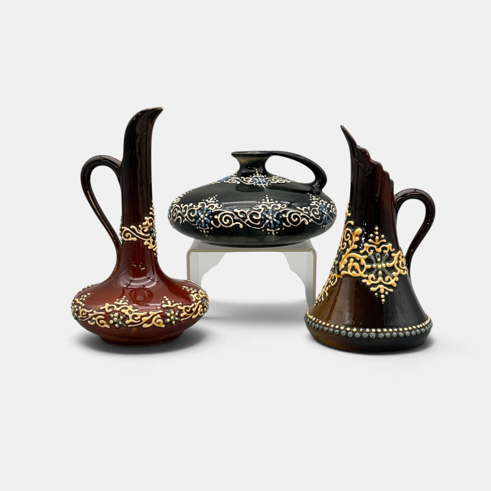 Three Weller Turada ewers various colors.: Three Weller Turada ewers, two with brown background and one with black. Various colors of slip trailing. None are marked. Height of the tallest is 6 7/8 inches.