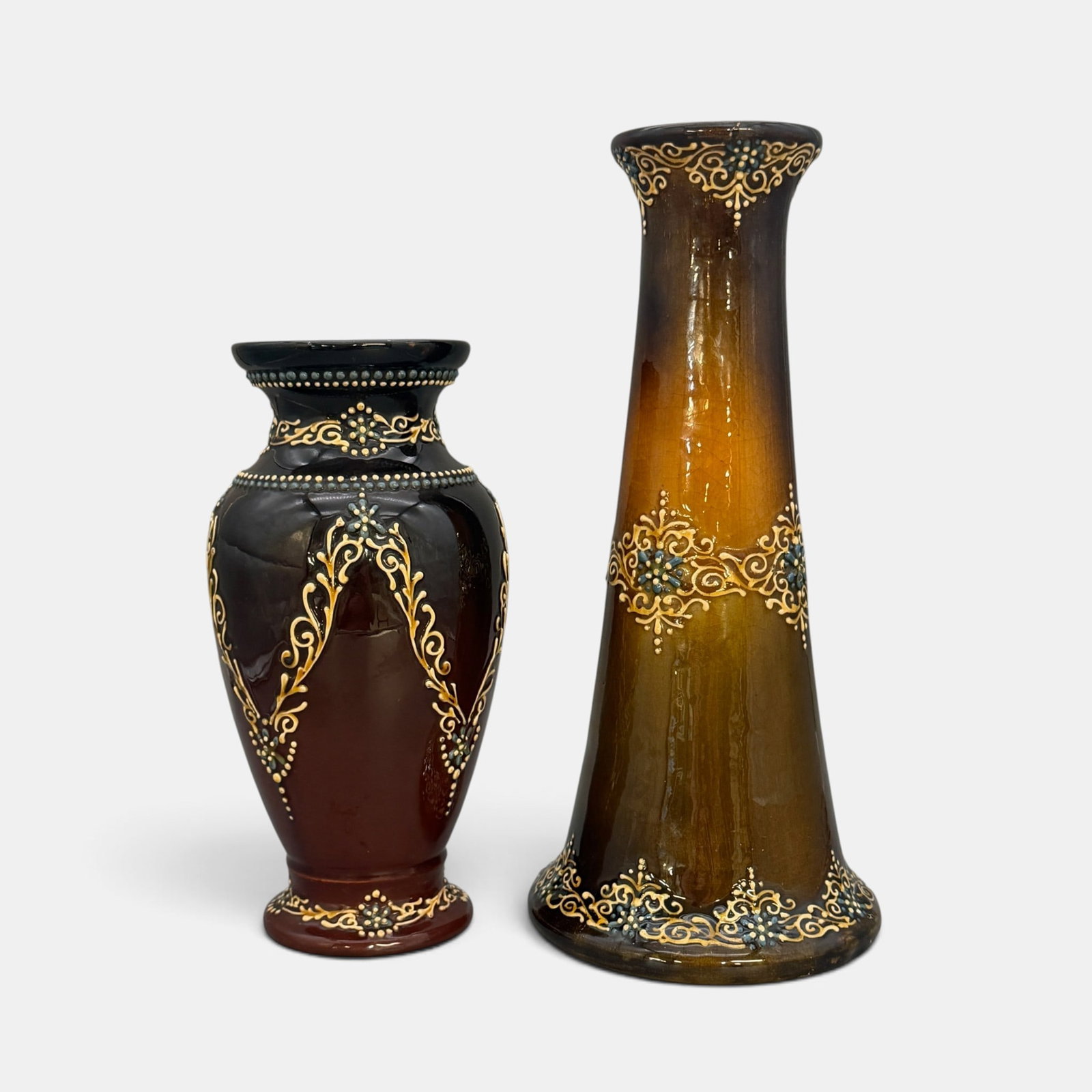 Two Weller Turada vases, brown ground, blue and cream slip.: Two Weller Turada vases with a dark brown ground and blue and cream slip trailing. Both unmarked. Heights 13 3/4 and 10 1/2inches. inches. The 10 1/2 inch vase bears a Just Art Pottery silver label.