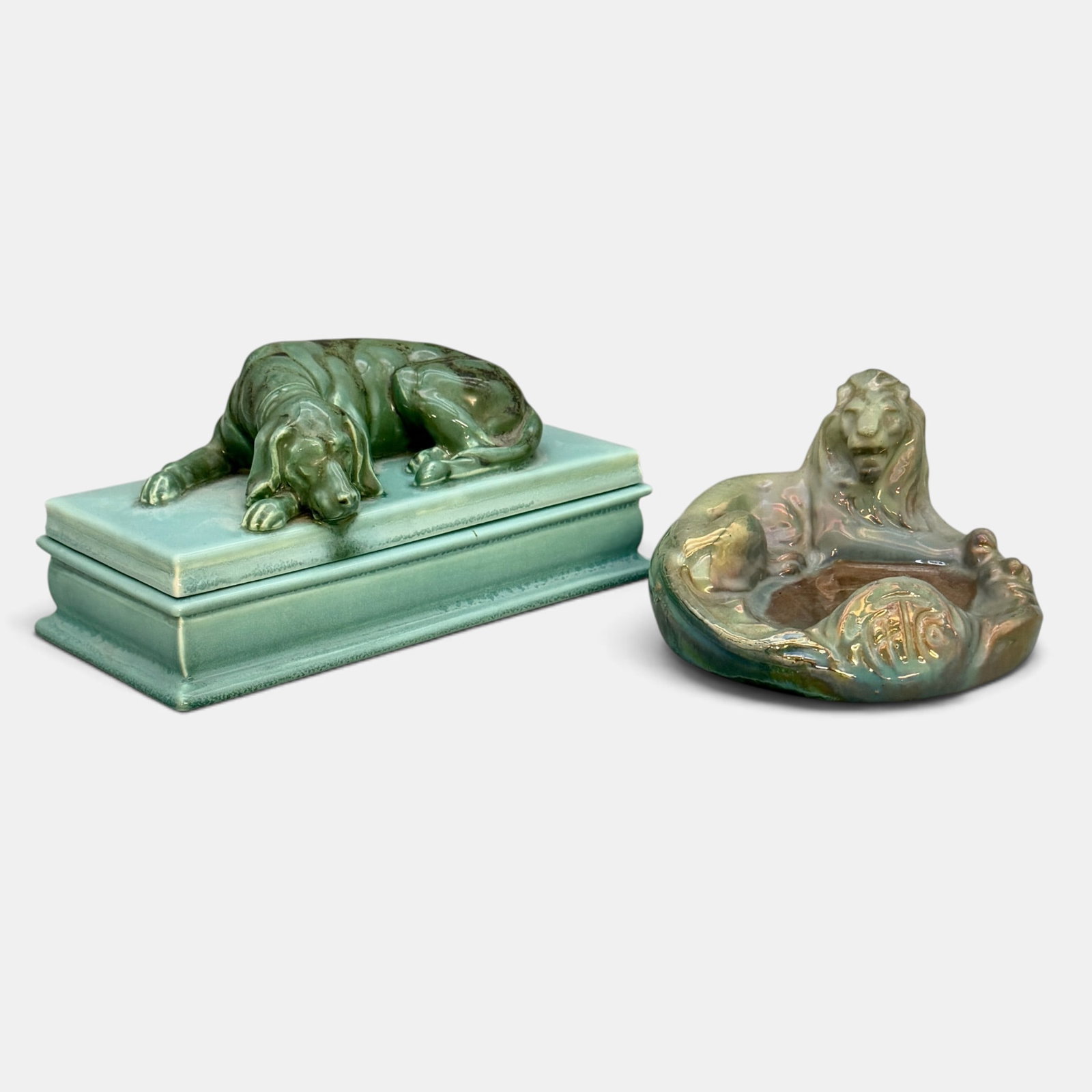 Two Unusual Mosaic Tile Company items: Two unusual Mosaic Tile Company items. 1. Lion ashtray done in a gold-blue luster glaze. 2. Sleeping dog covered box with the dog done in green-black glaze and the box in a crystalline glaze. Both