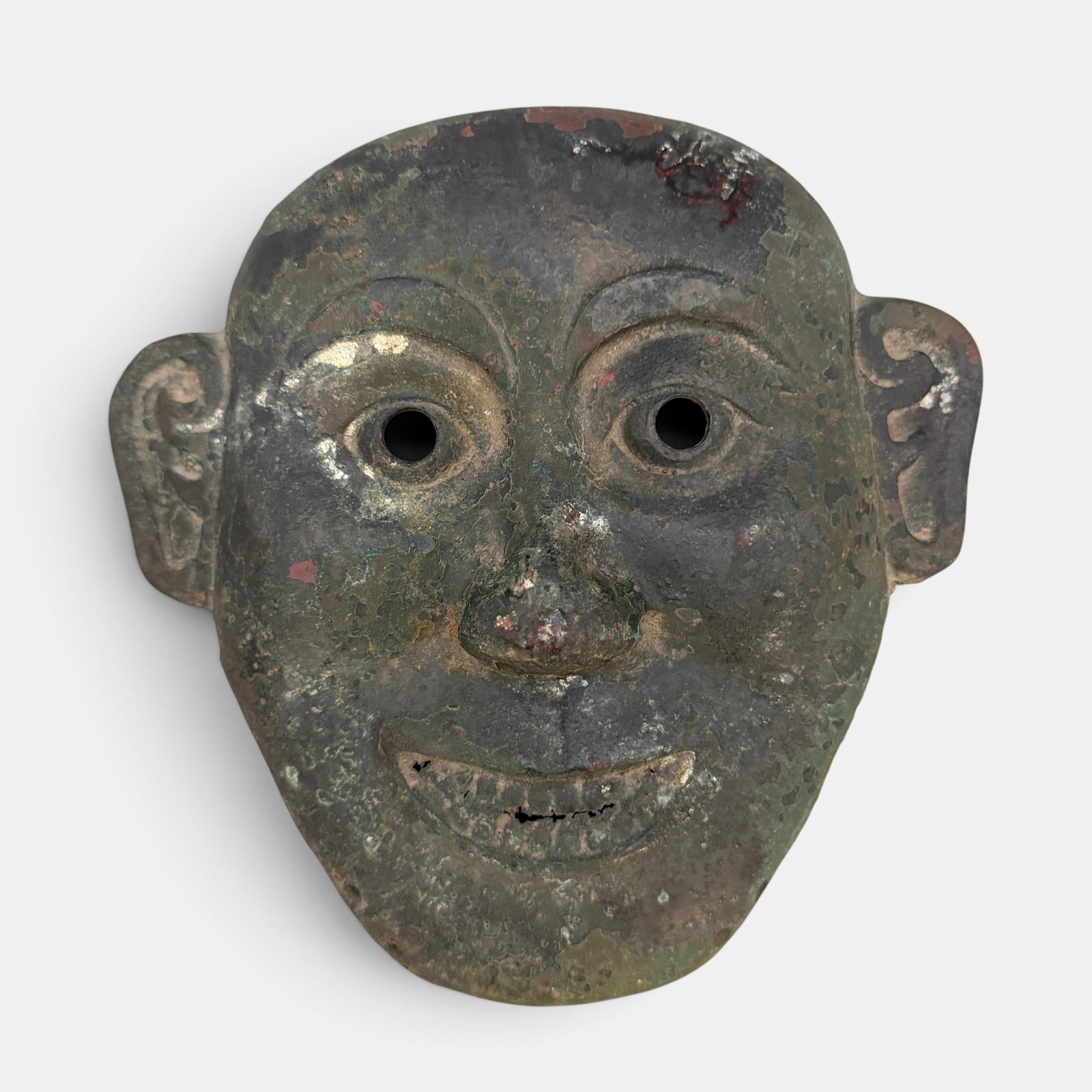 A Chinese Bronze Funerary Mask: Cast with a smile, depicting a pair of arched eyebrows above circular eyes and high cheekbones, the mouth open revealing the teeth. Property from the Collection of David Billings and Beverly Hall Bill
